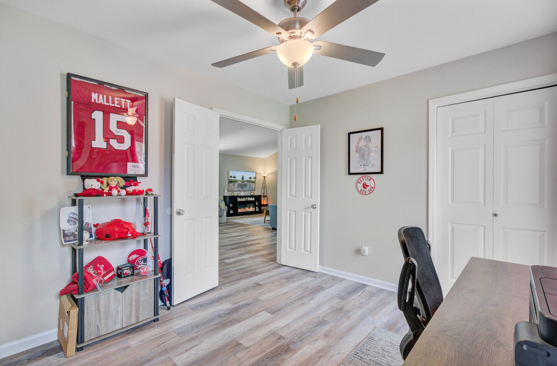 Home office with sports memorabilia, a ceiling fan, closet doors, and an open doorway to the living area.