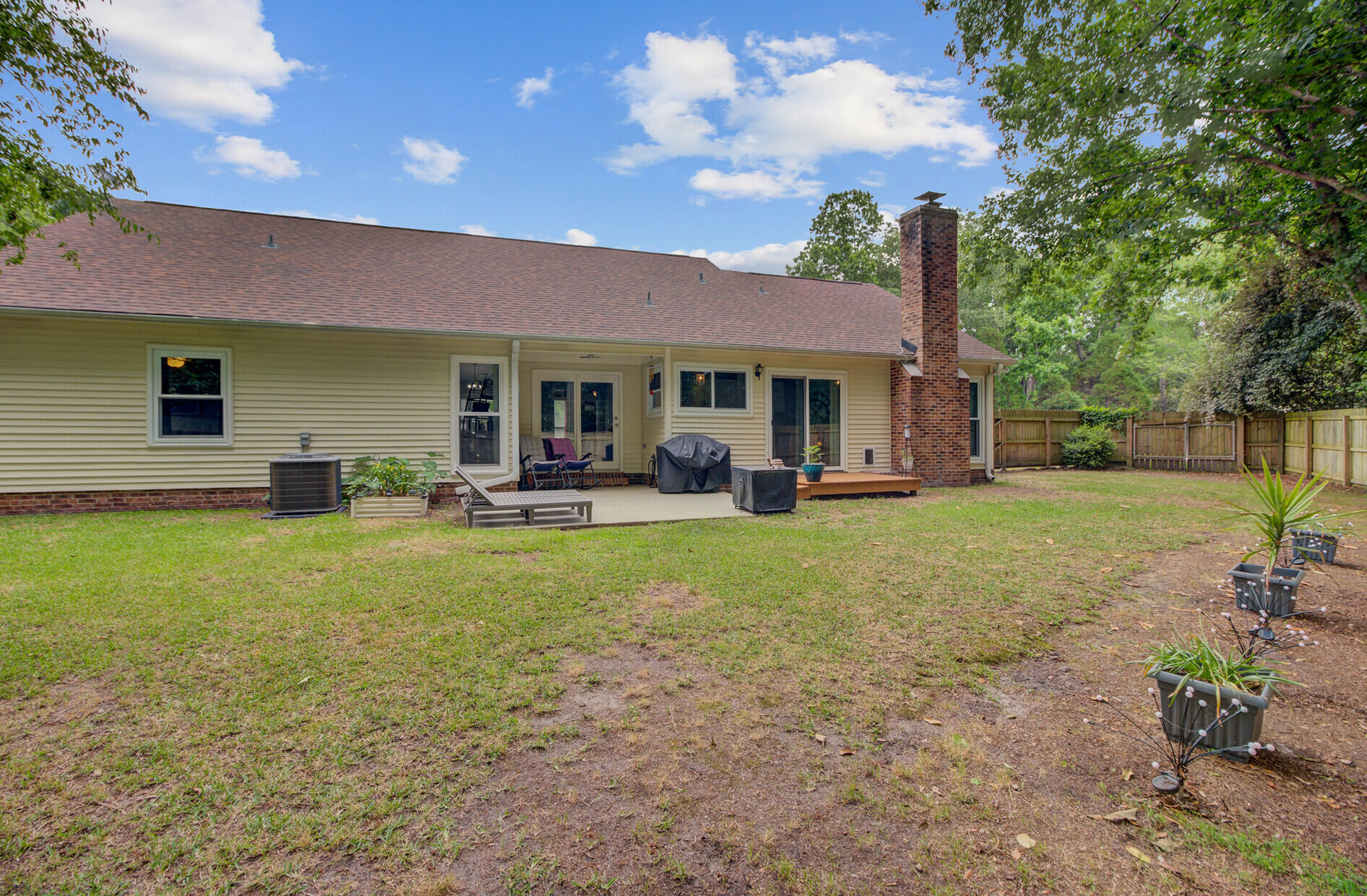 Home’s rear exterior with a brick chimney, patio, and fenced backyard.