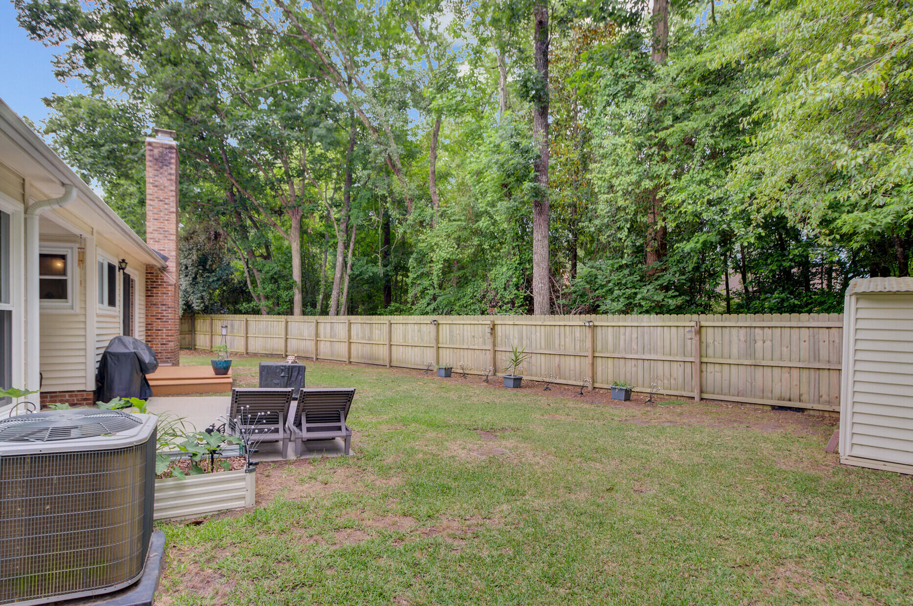 Backyard with a grassy lawn, wooden privacy fence, and mature trees behind the house.