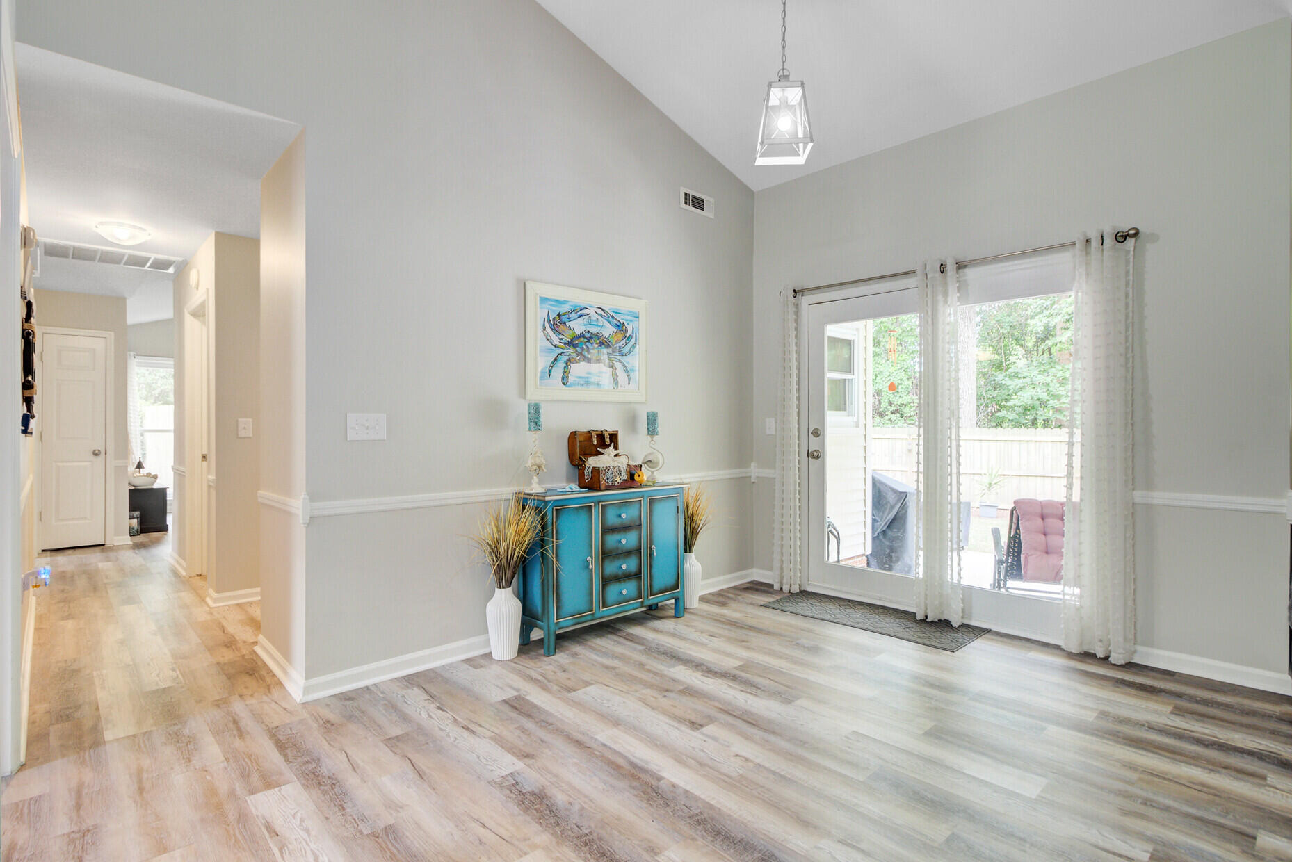 Bright interior with a turquoise console cabinet, tall curtained windows, and glass door to the backyard.