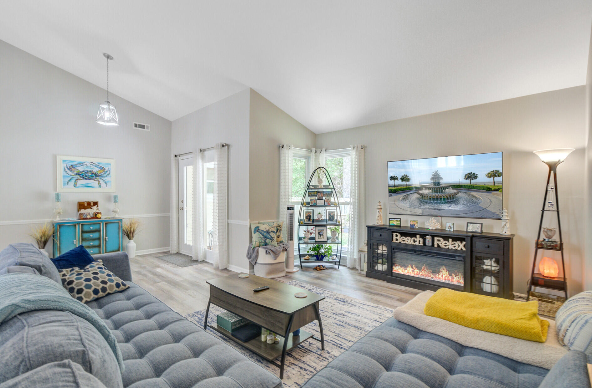 Furnished living room with gray sectional, vaulted ceiling, and black fireplace console.
