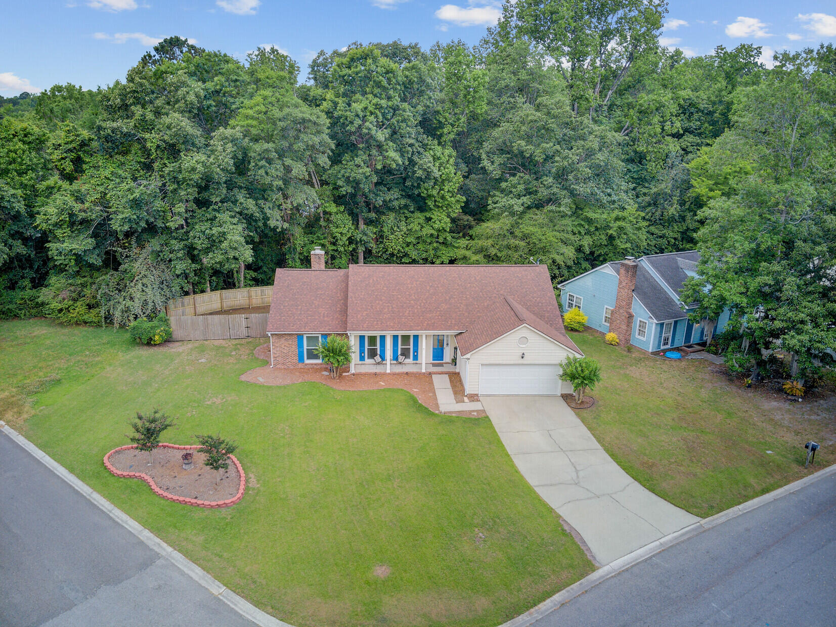 Aerial view of a single-story home with a broad lawn and wooded backdrop.