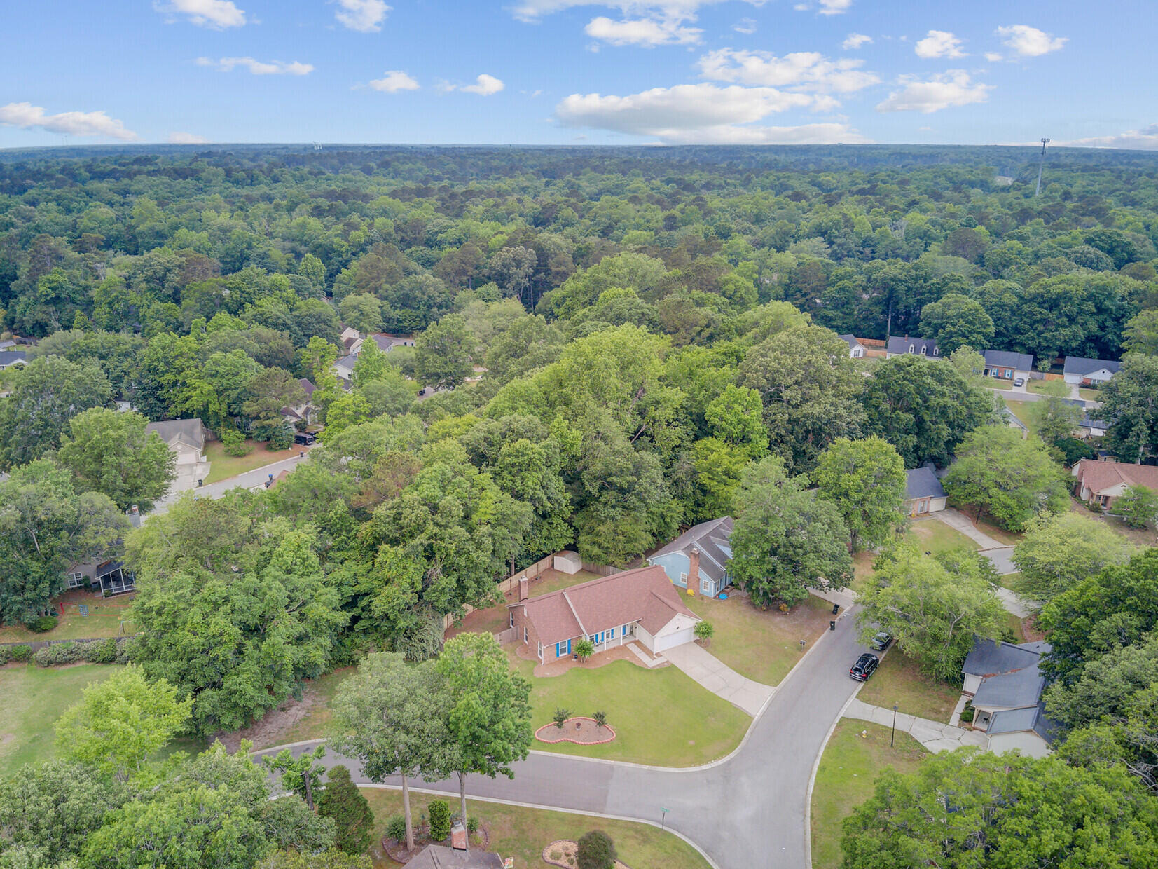Aerial view of a home surrounded by mature trees, neighboring houses, and extensive woodland.