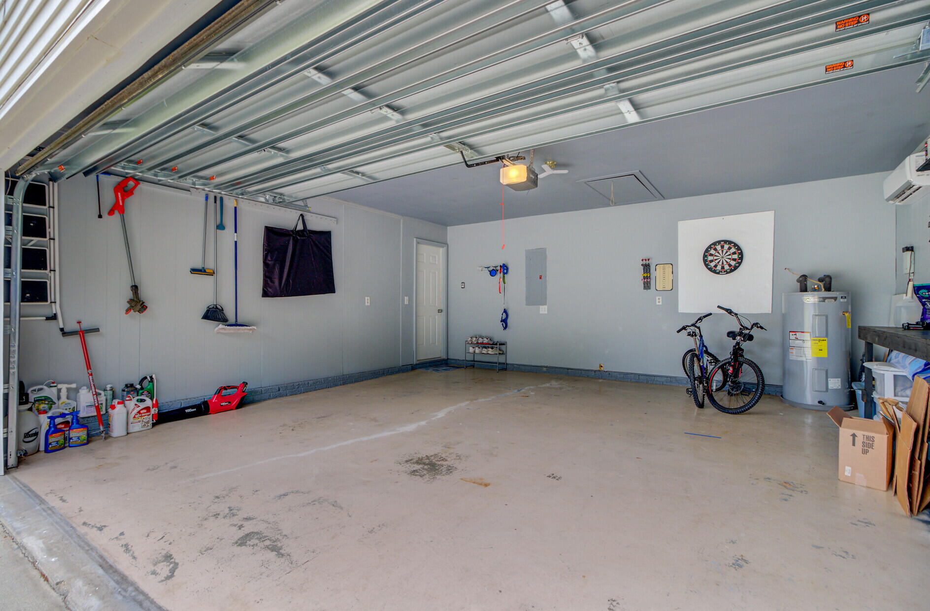 Spacious garage with a raised overhead door, dartboard, bicycles, and a water heater.