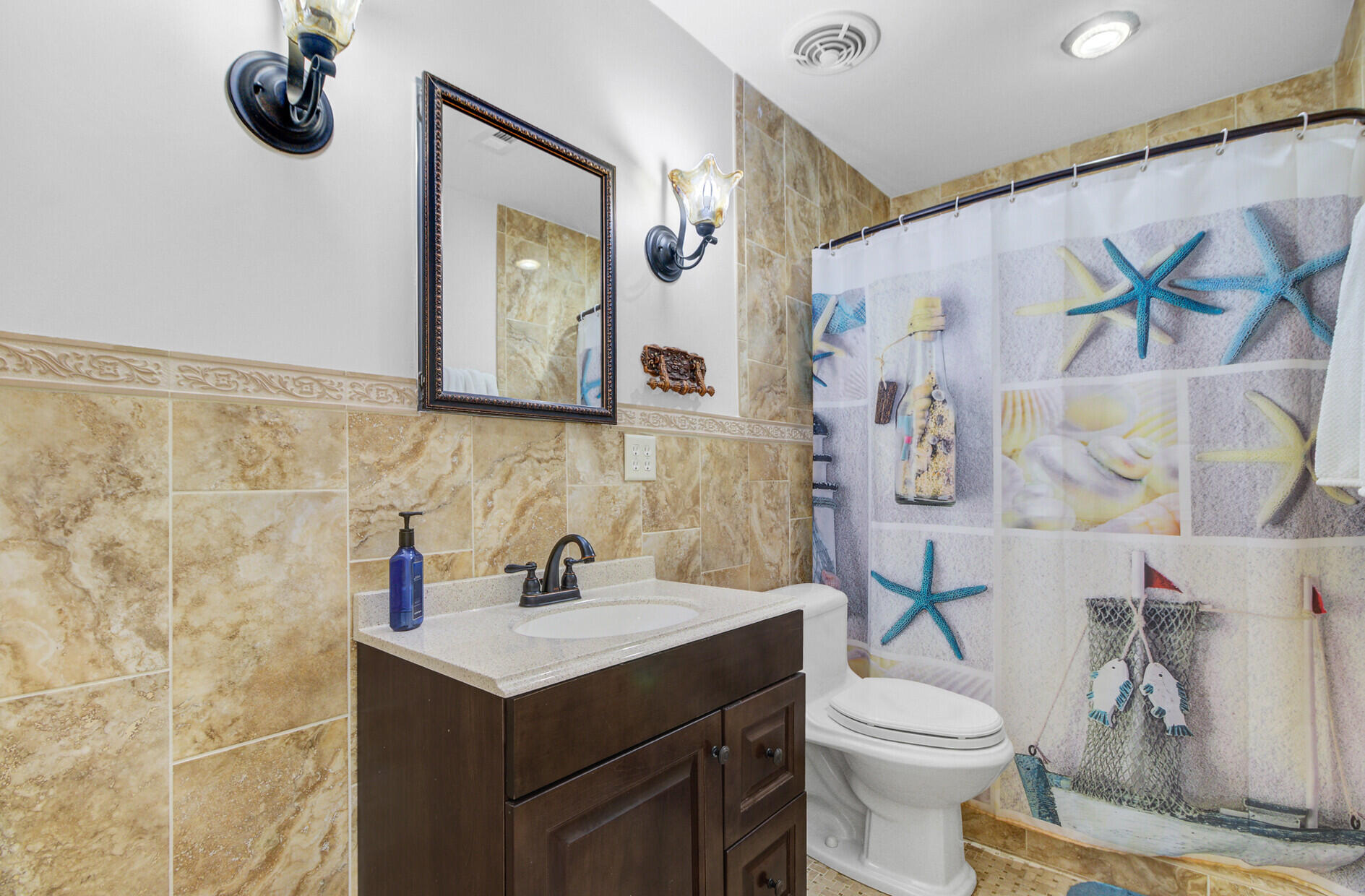 Bathroom with a dark wood vanity and tan tile, plus a starfish-and-shell shower curtain.