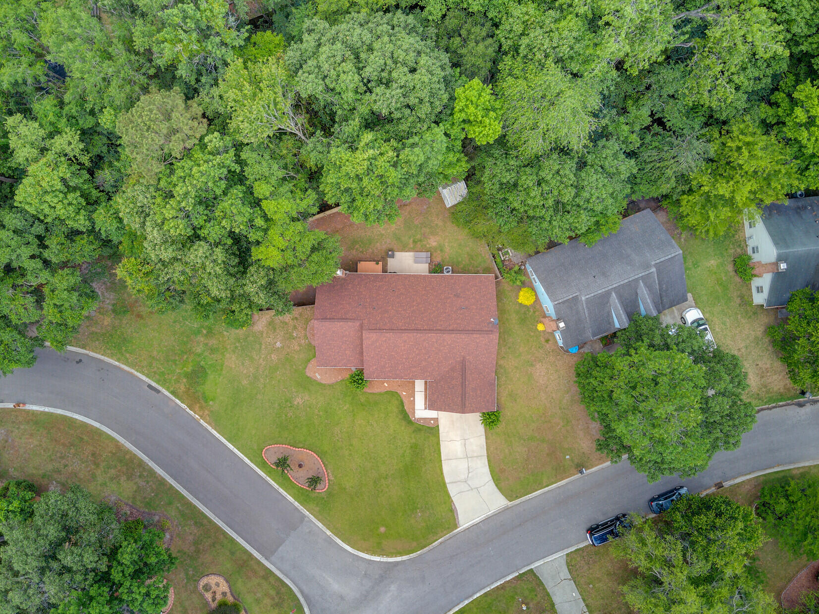 Aerial view of a red-roofed home with a driveway, lawn, and wooded backyard.