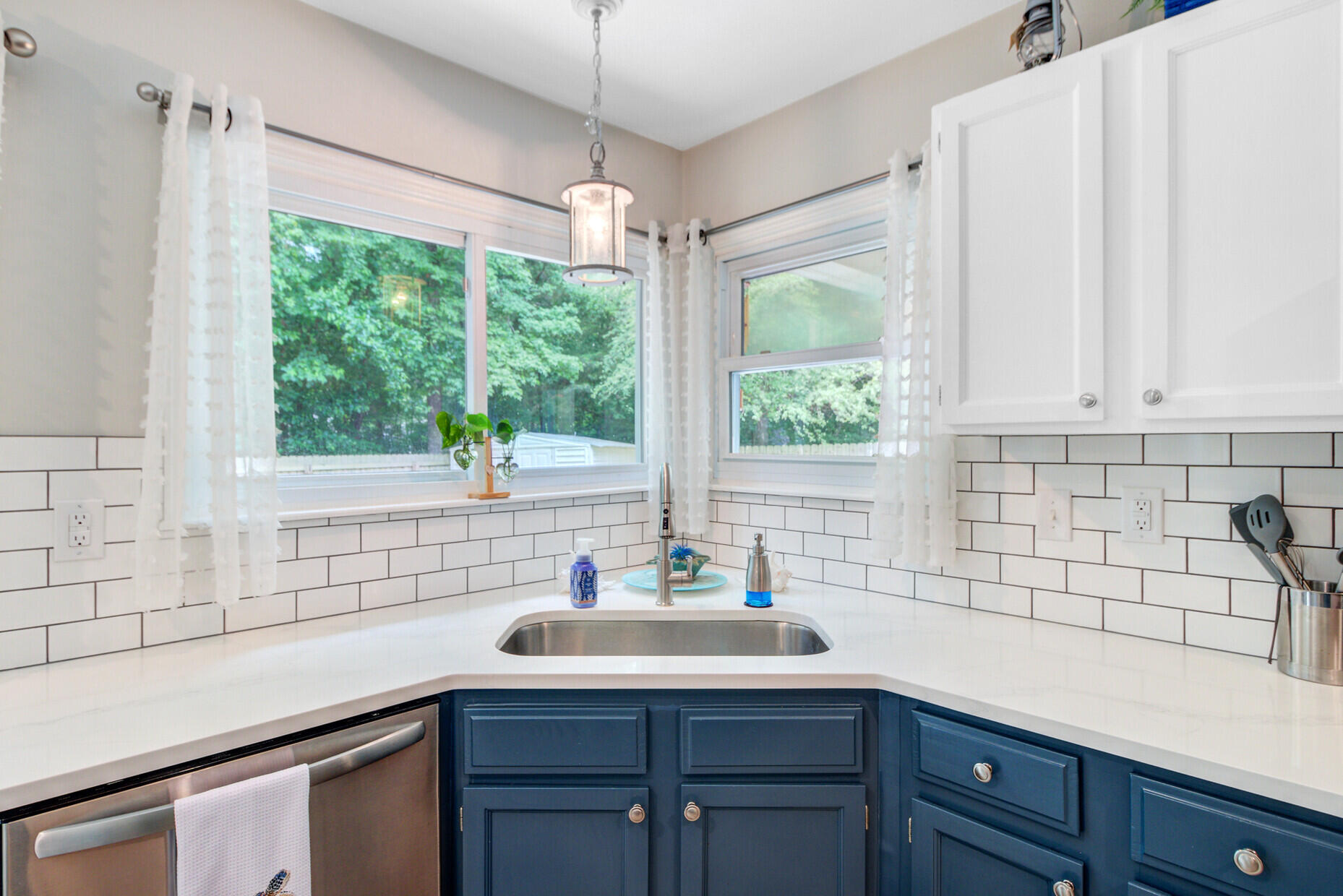 Kitchen with blue cabinets, white subway tile, and a corner sink beneath two windows.