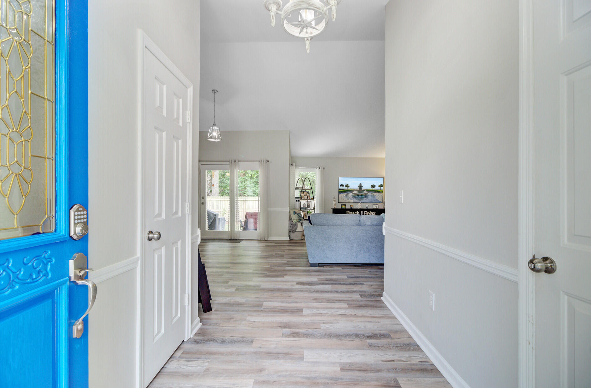 Entry hall opening into a living room, with a bright blue front door and gray plank flooring.