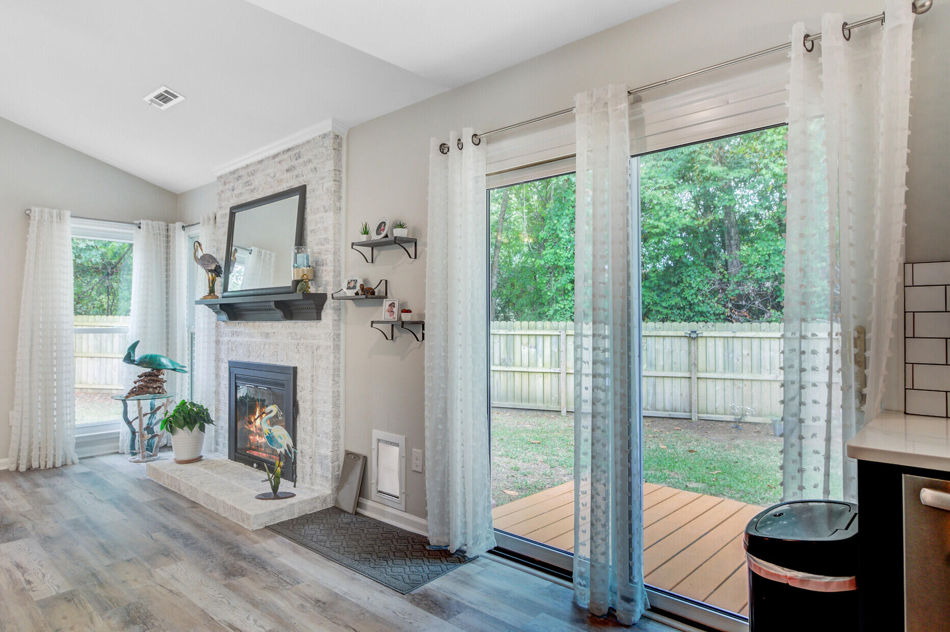 Living room with a white brick fireplace and sliding glass doors overlooking a fenced backyard.
