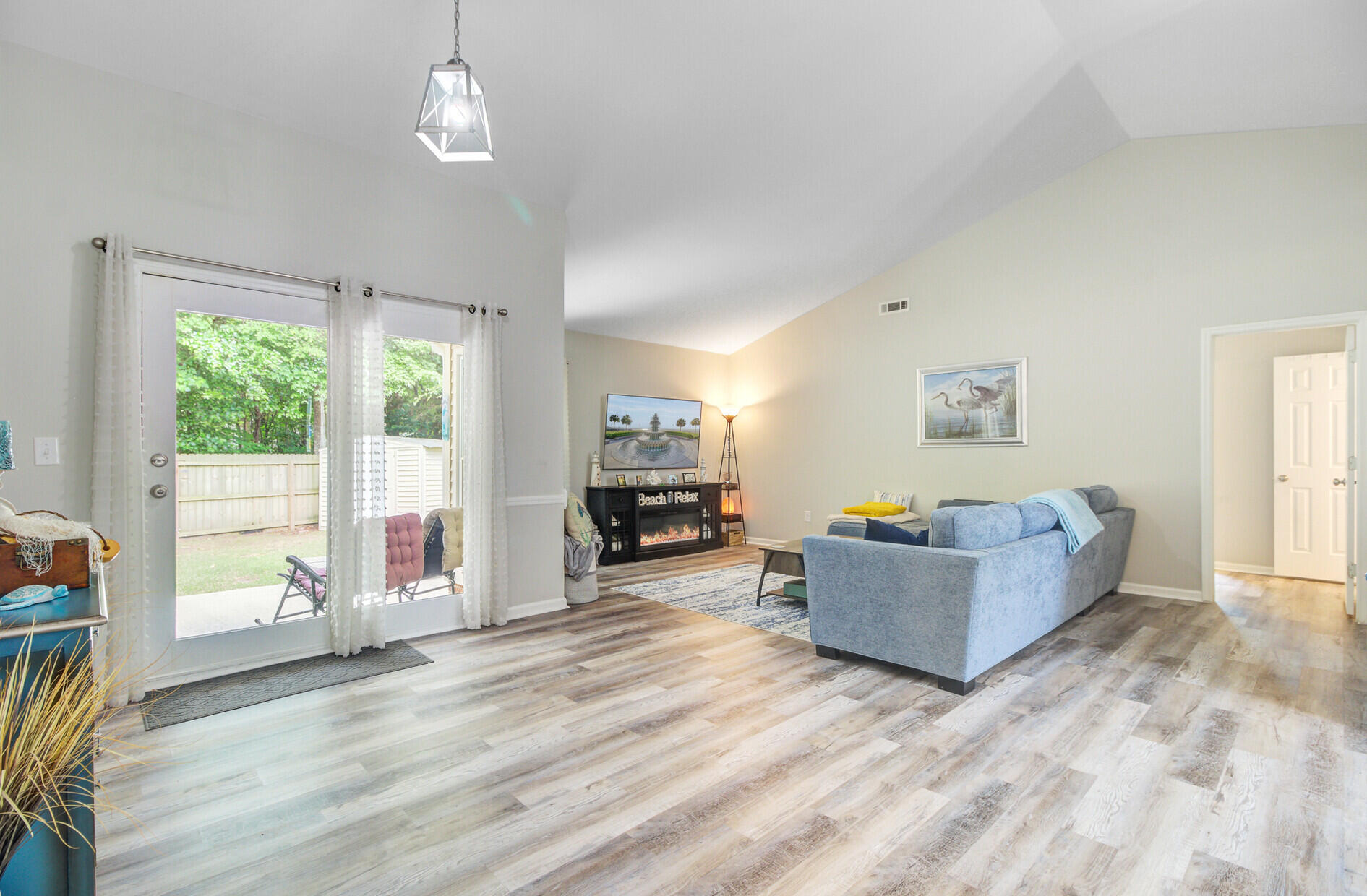 Living room with a gray sectional, fireplace, vaulted ceiling, and glass doors opening to a fenced yard.