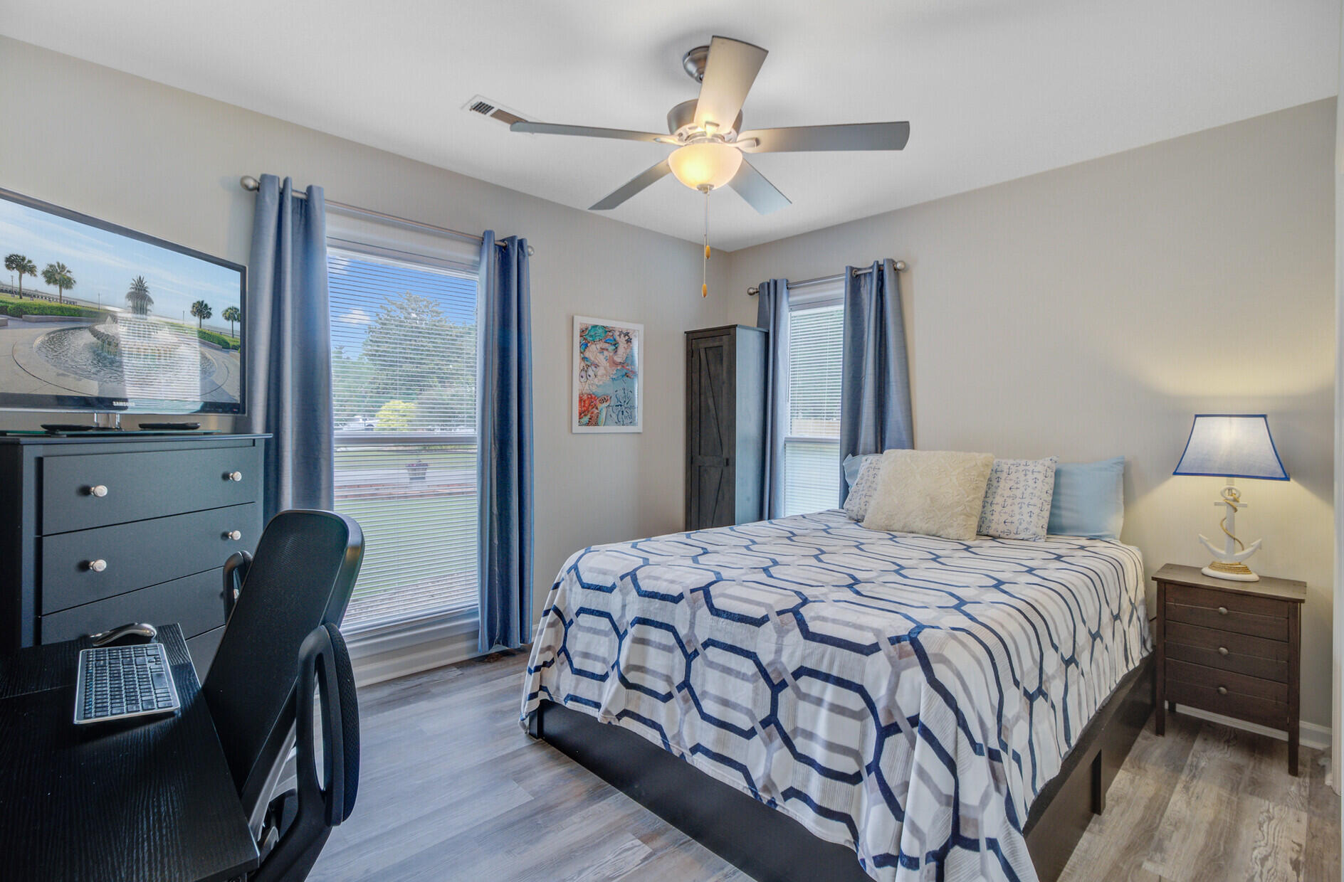 Furnished bedroom with a blue geometric-patterned bedspread, desk, and ceiling fan.