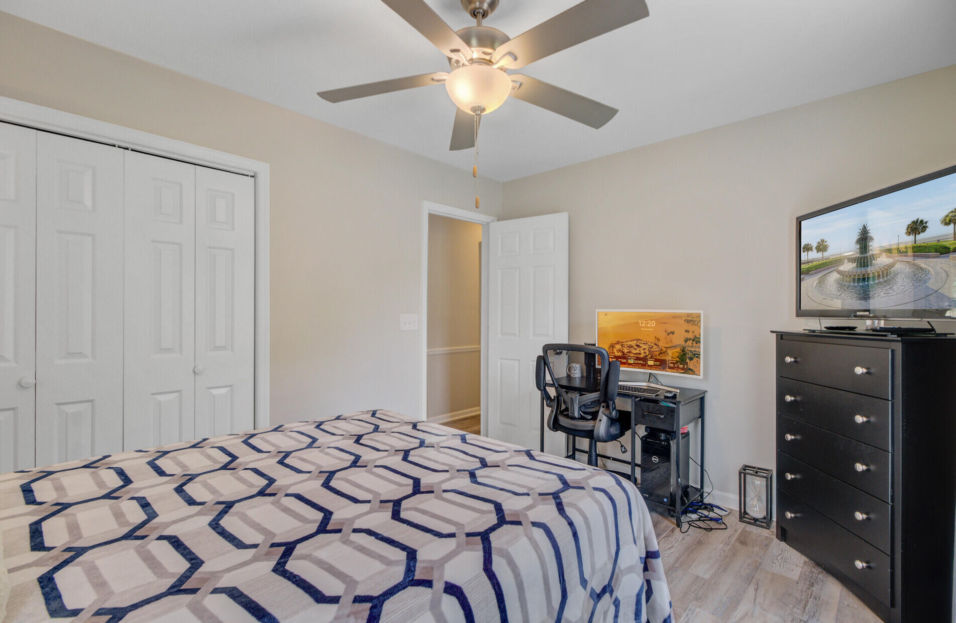 Furnished bedroom with a geometric-patterned bed, ceiling fan, and desk workstation.