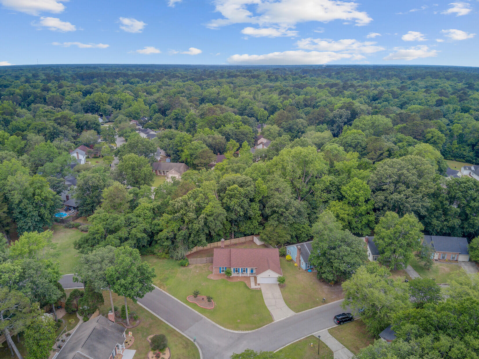 Aerial view of a home on a curving neighborhood street, surrounded by mature trees and nearby houses.