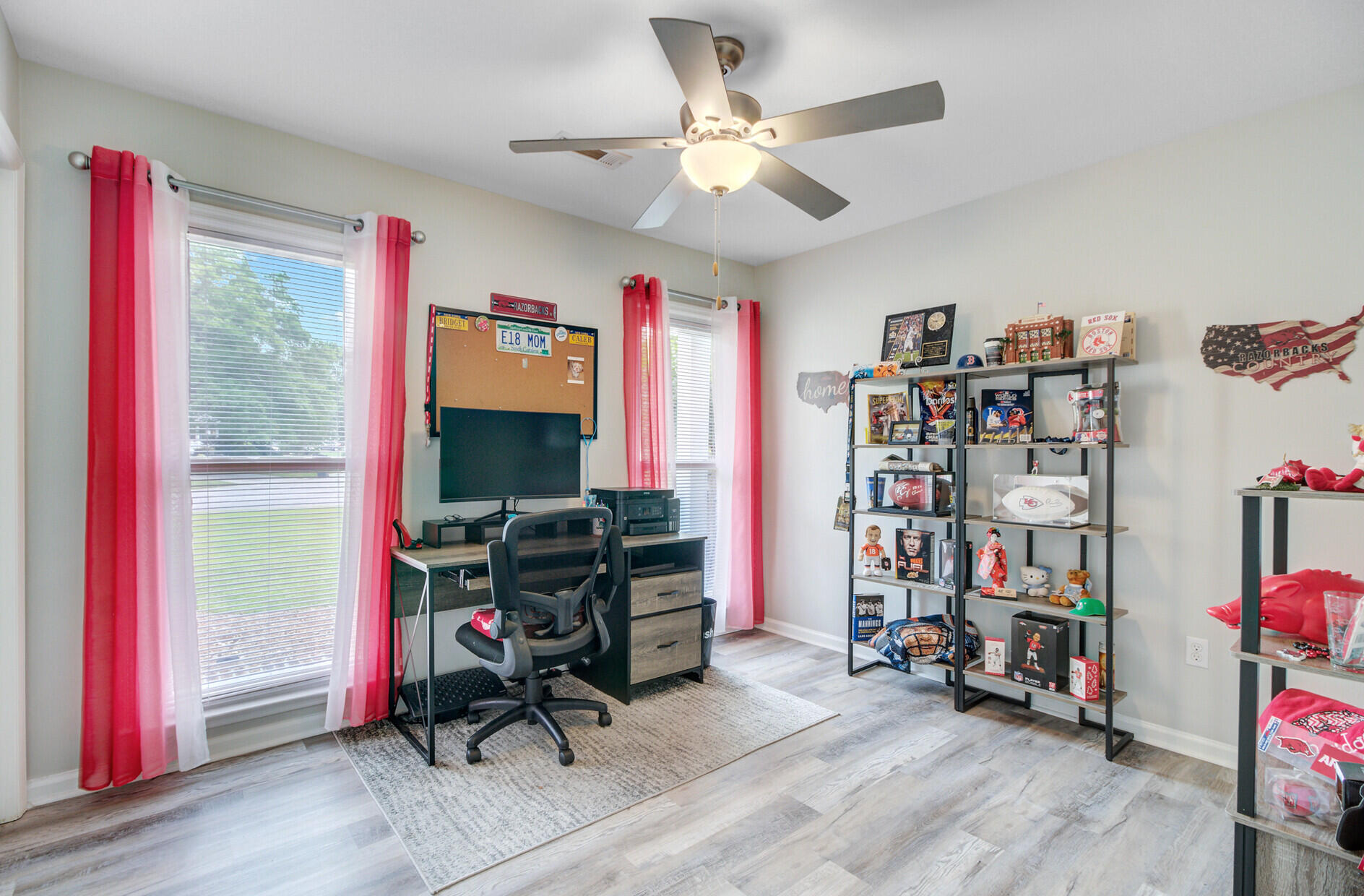 Home office with red curtains, a computer desk, and shelves of sports memorabilia.