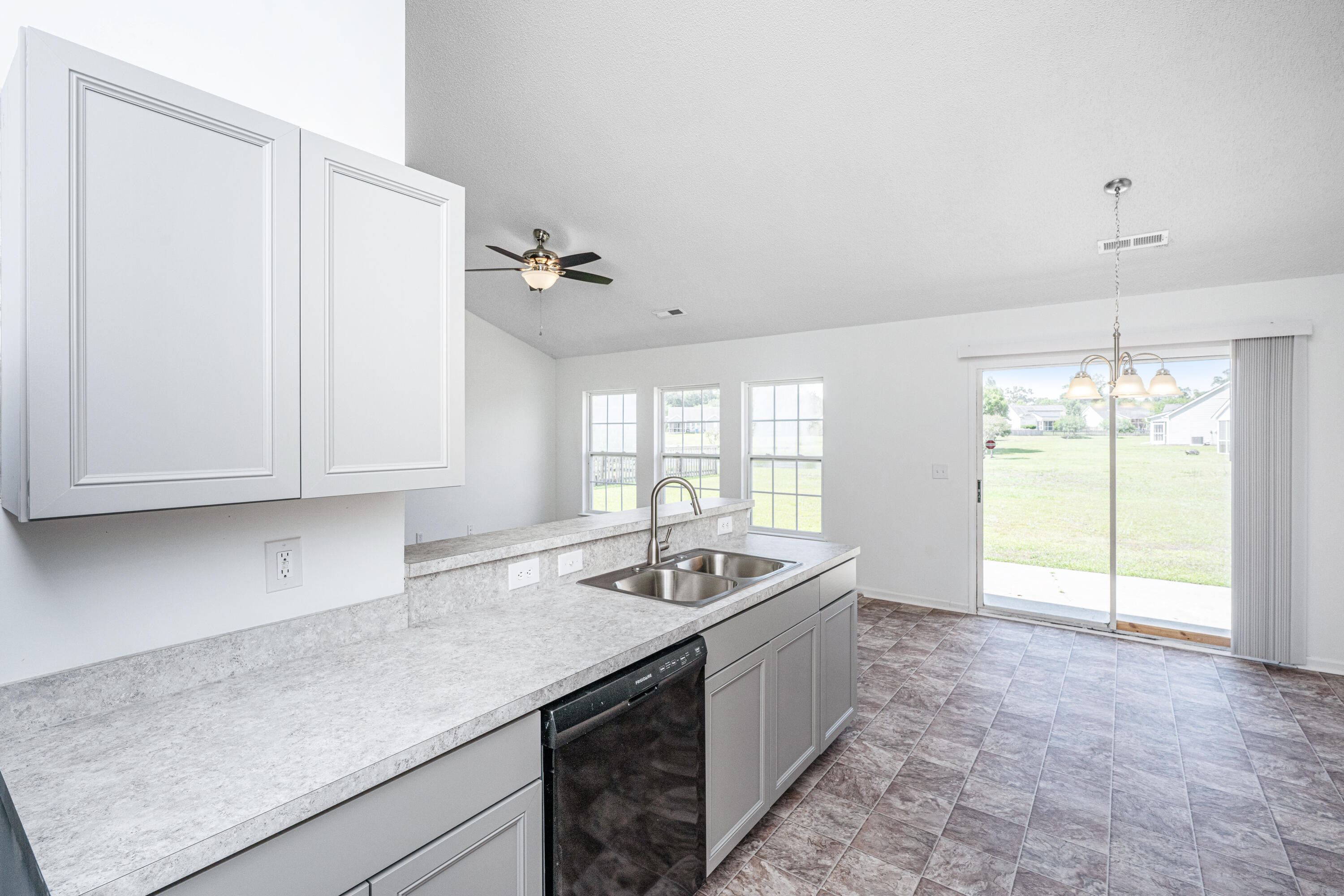 Vacant kitchen with white cabinets, a double-basin sink, and a sliding glass door to the lawn.