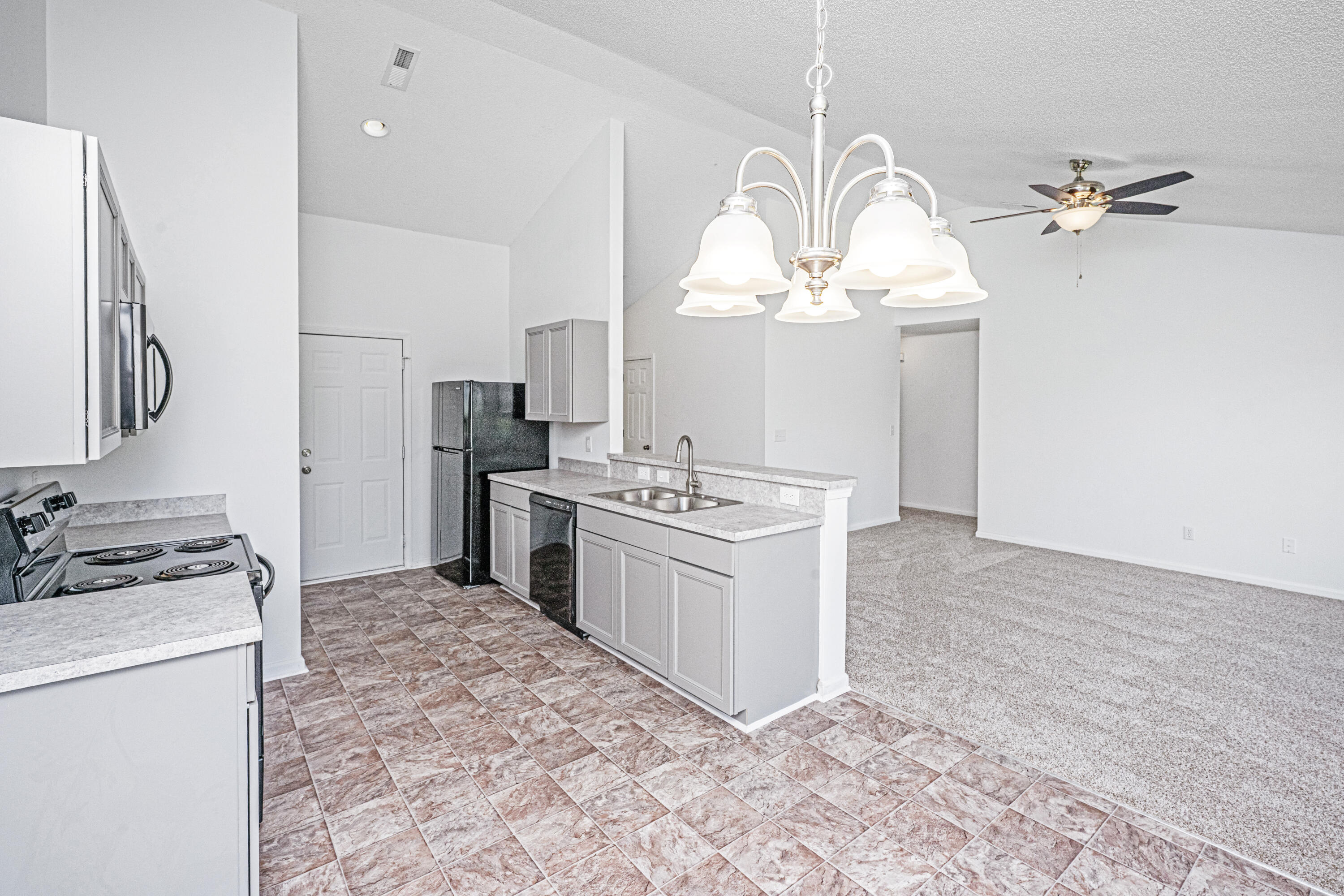 Open kitchen with white cabinets, a sink peninsula, patterned tile flooring, and adjoining carpeted living area.