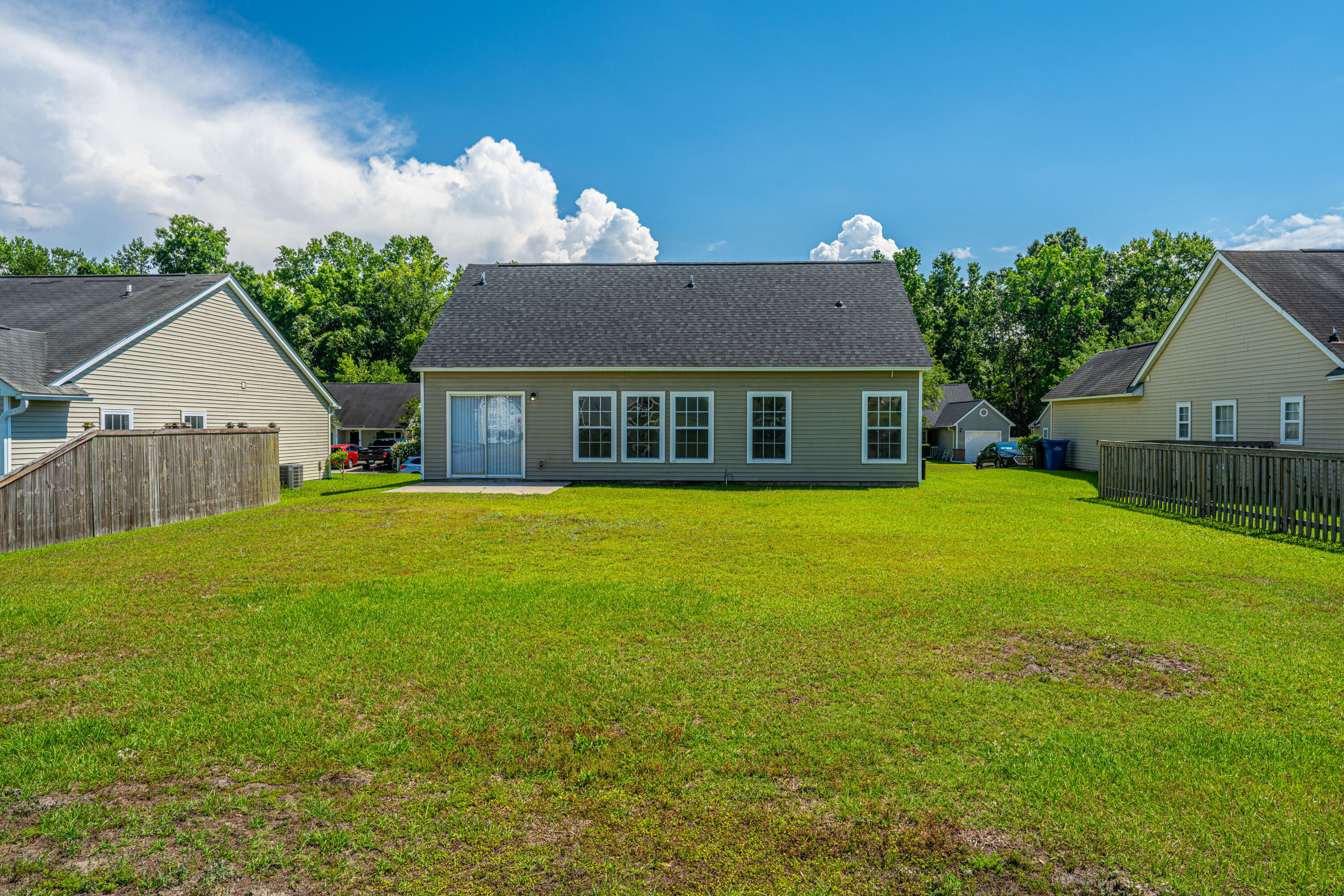 Rear of a gray-sided home with a broad grassy backyard and sliding glass door.