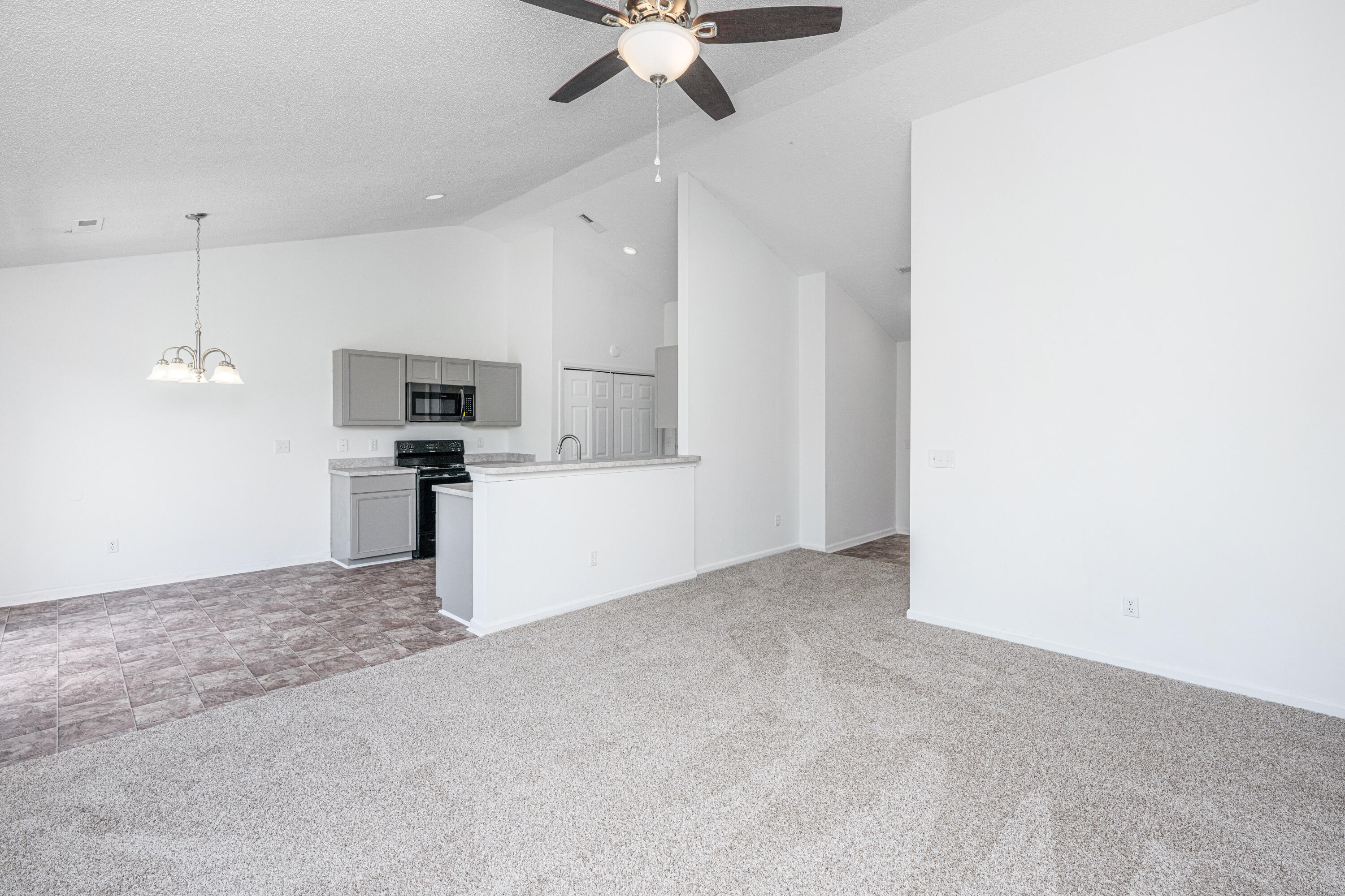 Open-plan kitchen and living area with a breakfast bar, gray cabinets, and mixed tile and carpet flooring.