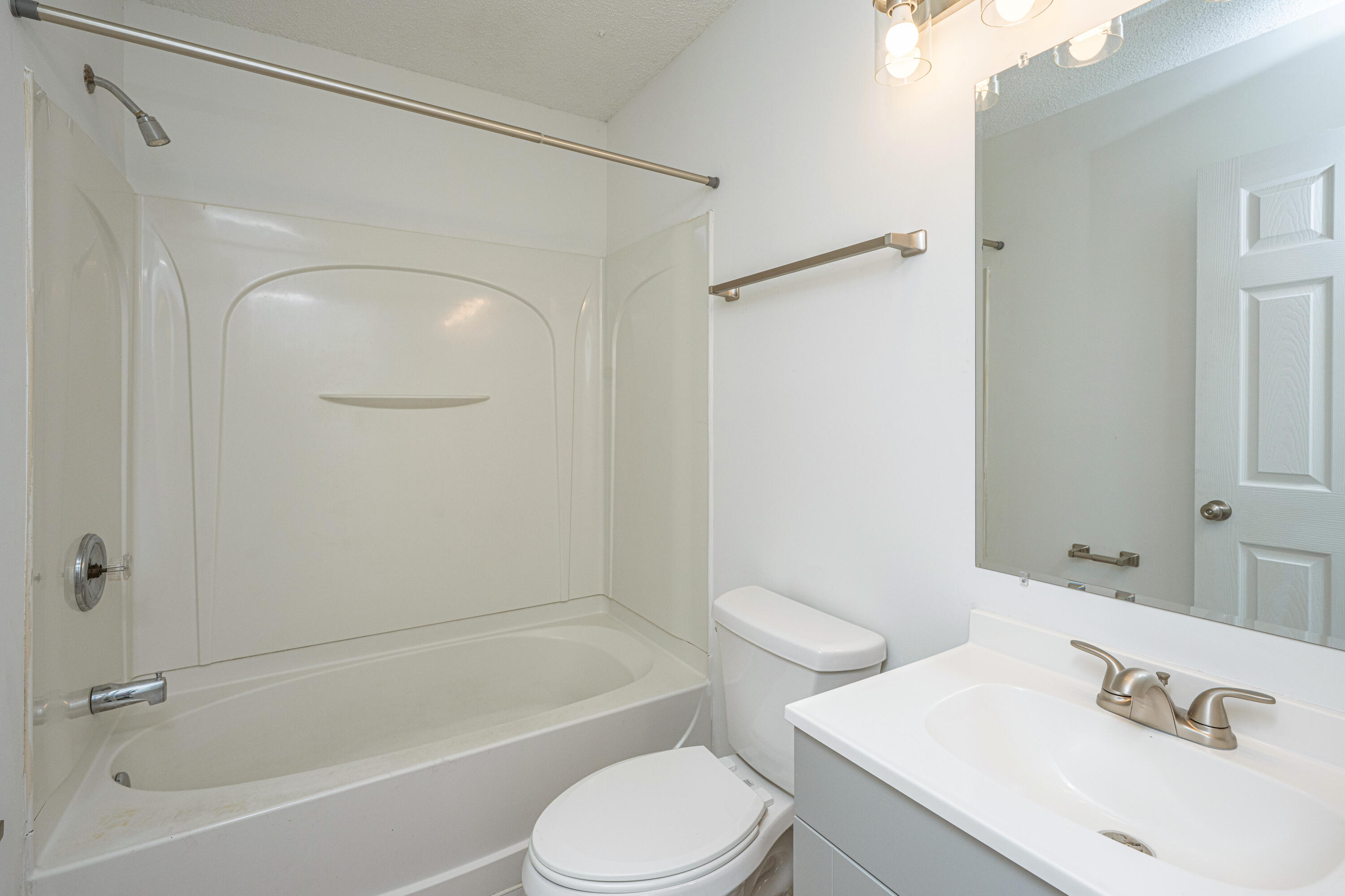 Bathroom with a white tub and shower, toilet, and vanity beneath a large mirror.