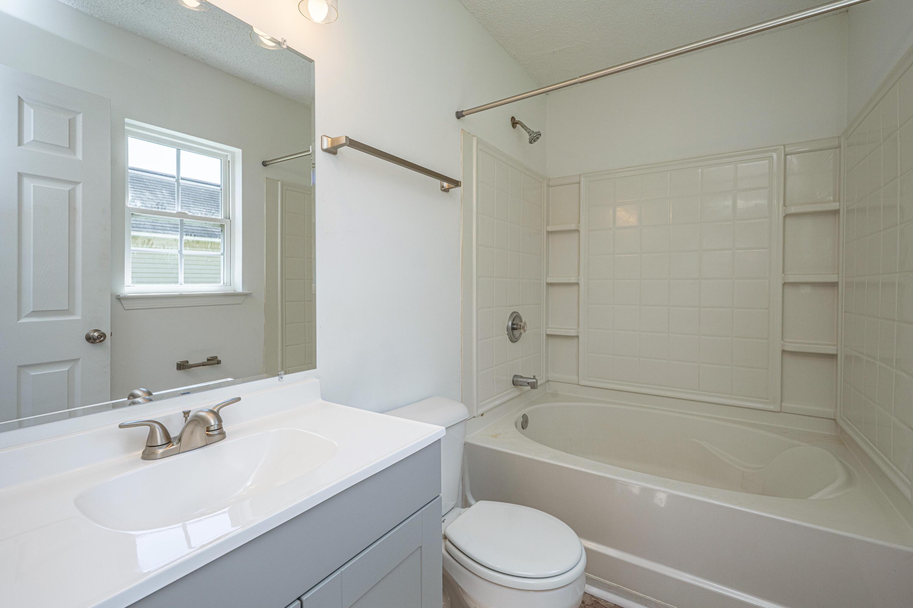 Bathroom with a white vanity, toilet, and bathtub with tiled shower surround and built-in shelves.