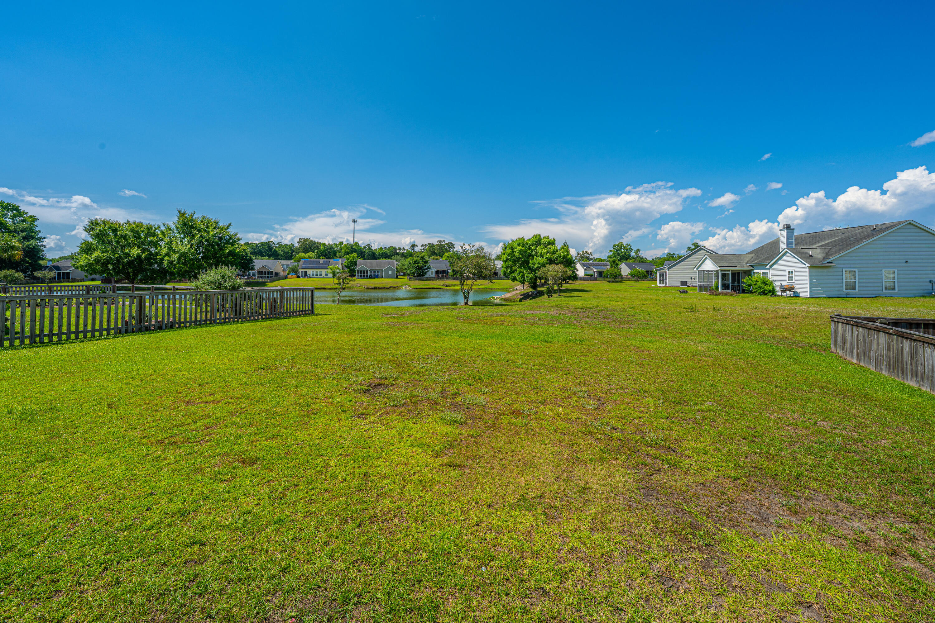 Spacious backyard lawn overlooking a pond, with wooden fencing and neighboring homes.