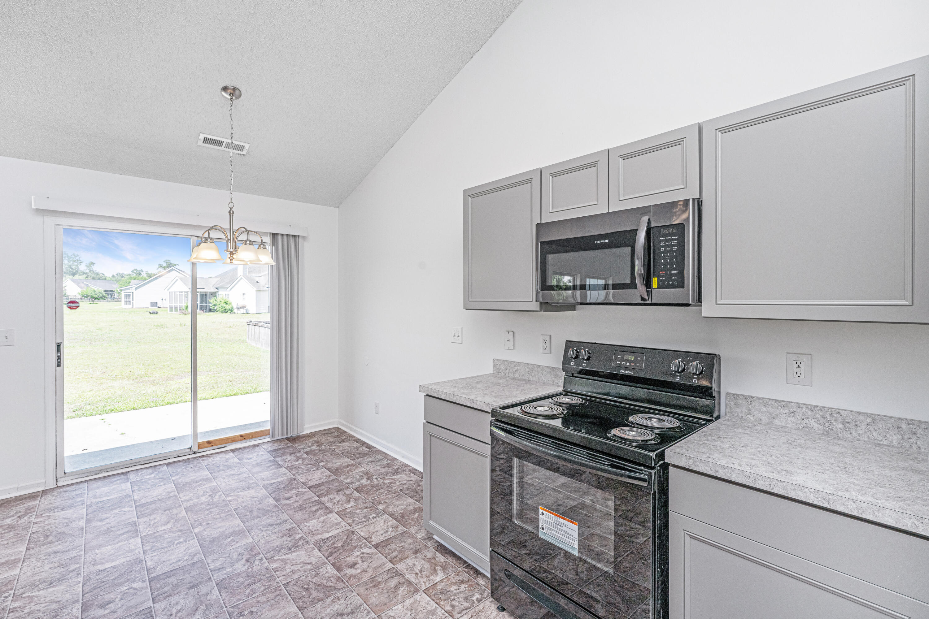 Kitchen with gray cabinets, black appliances, tiled floor, and a sliding glass door to the backyard.