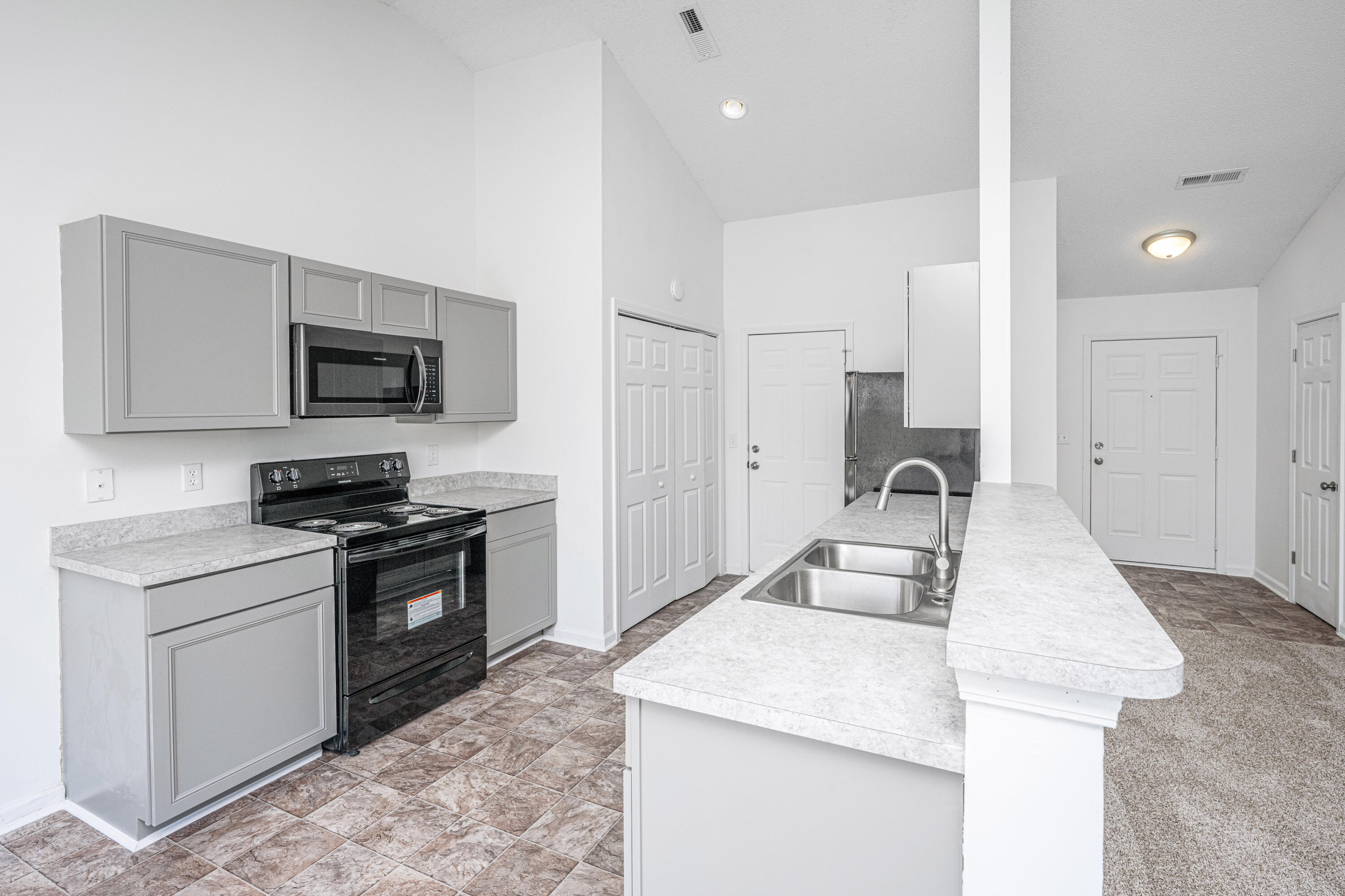 Kitchen with gray cabinets, black appliances, and a long island with a double-basin sink.