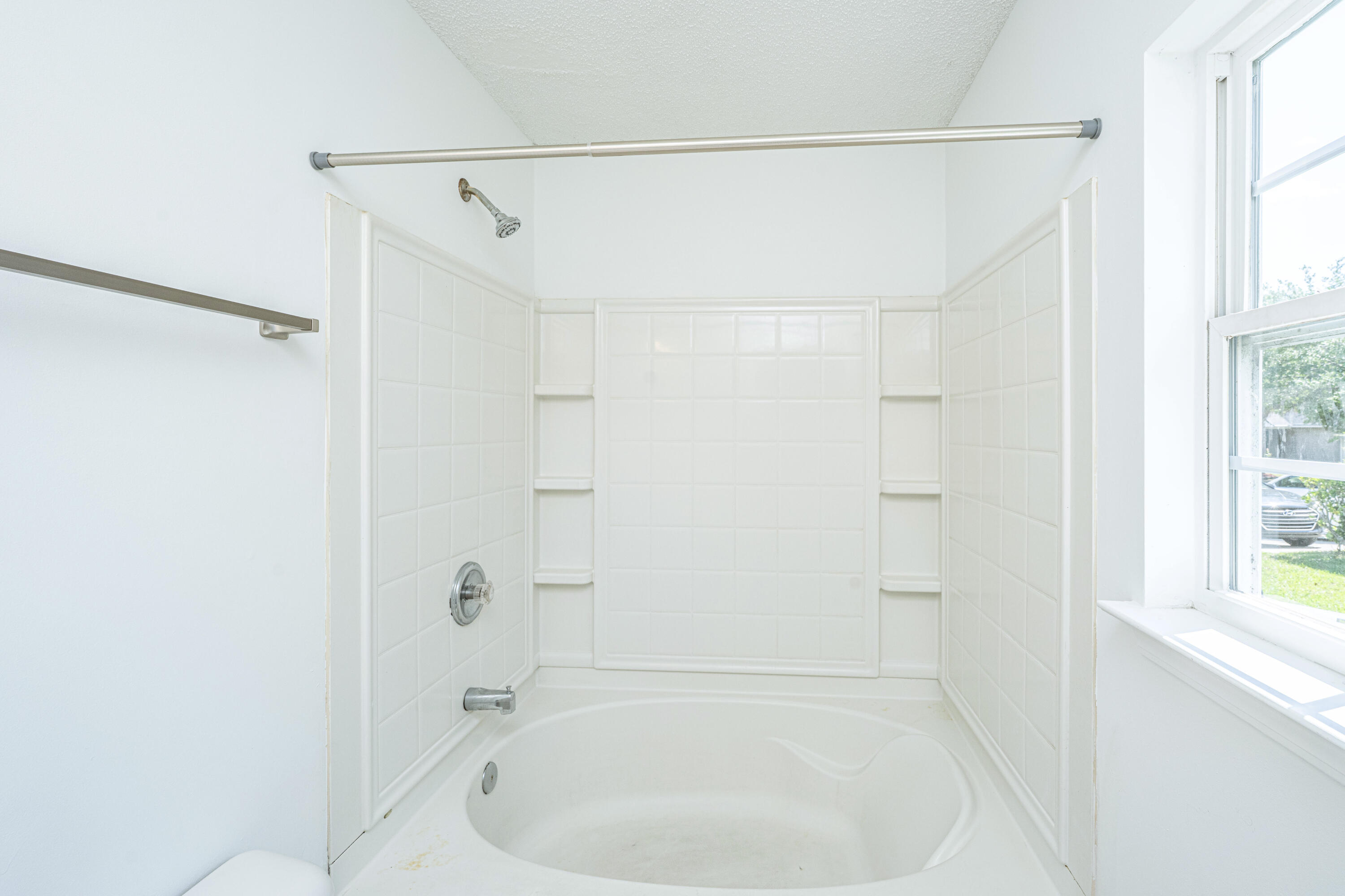 White bathtub and tiled shower with built-in shelves beside a bright window.