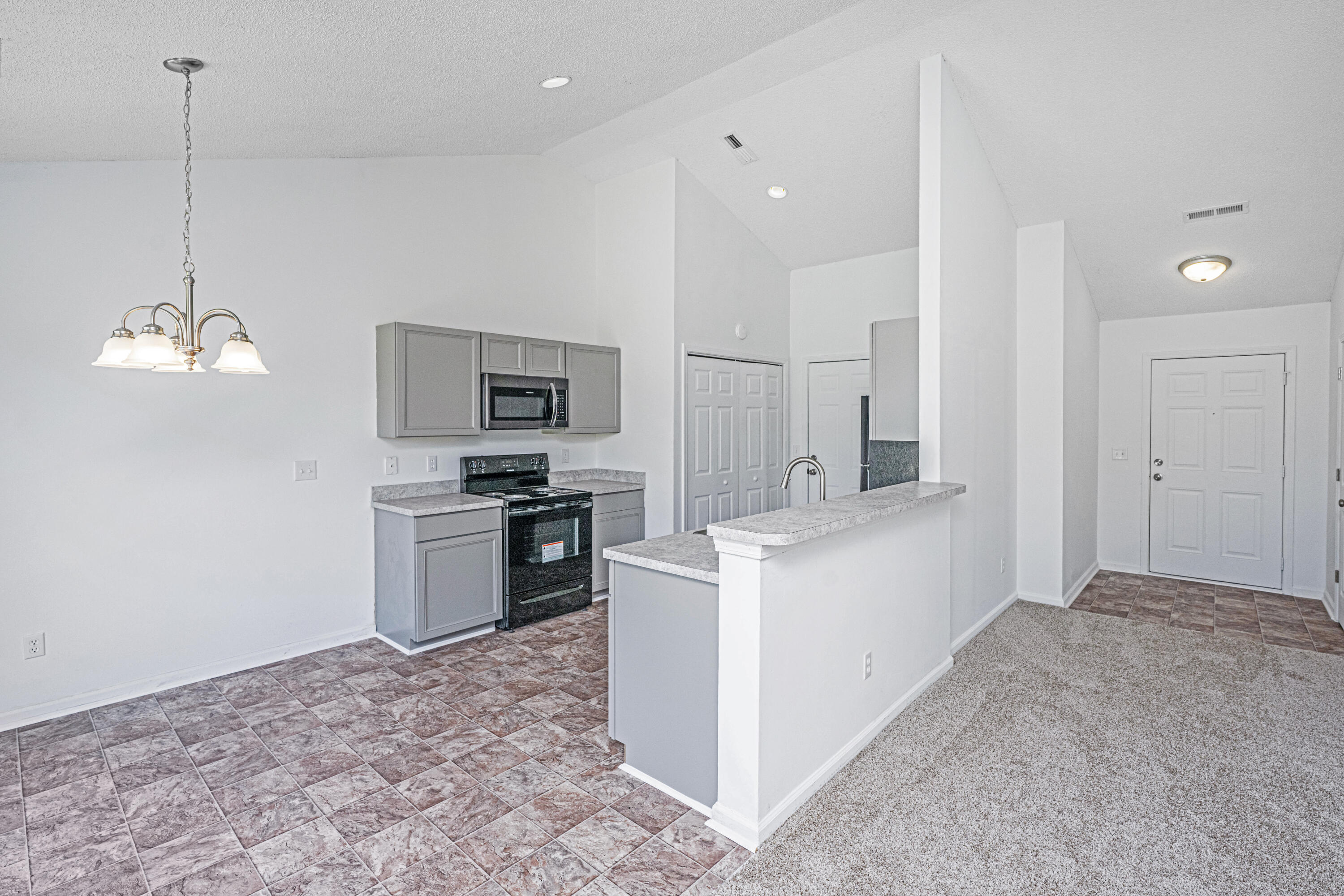 Open kitchen with gray cabinets, black appliances, a raised breakfast bar, and tile flooring beside the carpeted entry.