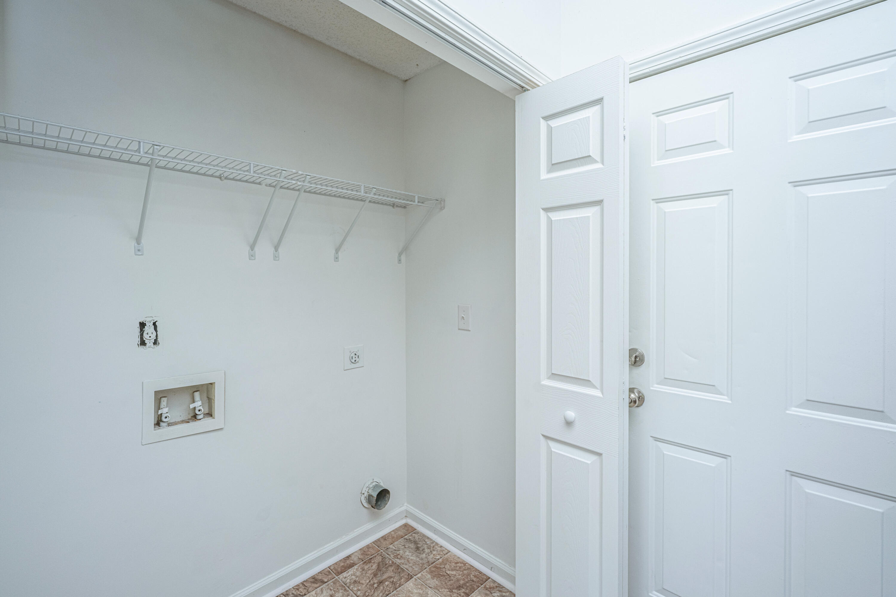 Empty laundry room with appliance hookups, a wire shelf, and a tiled floor.