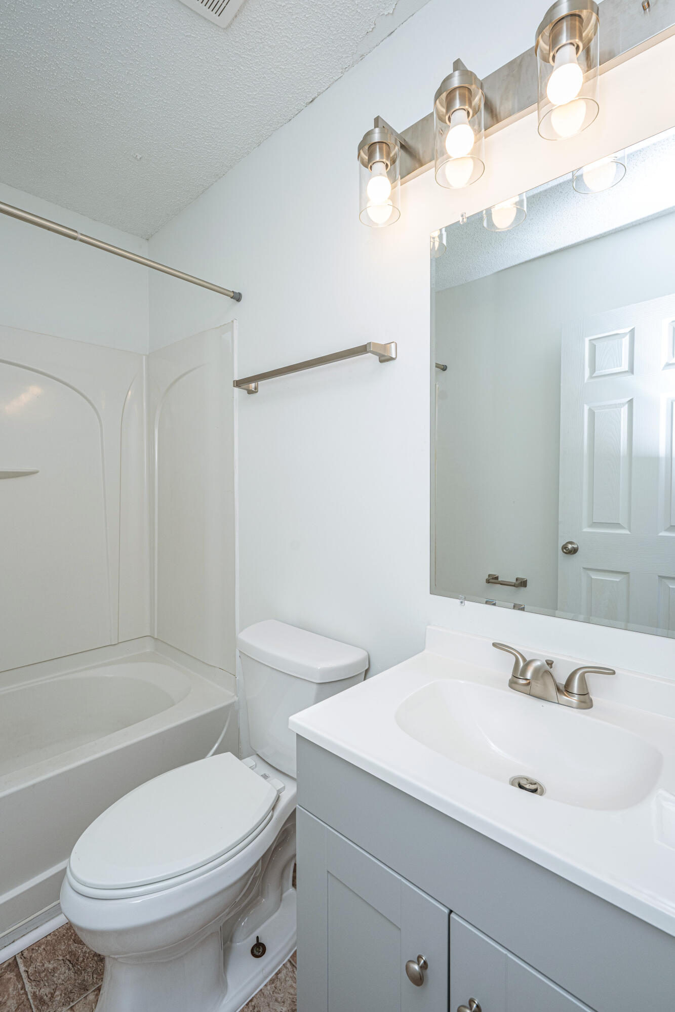 Bathroom with a tub-shower, toilet, and white vanity beneath a large mirror.