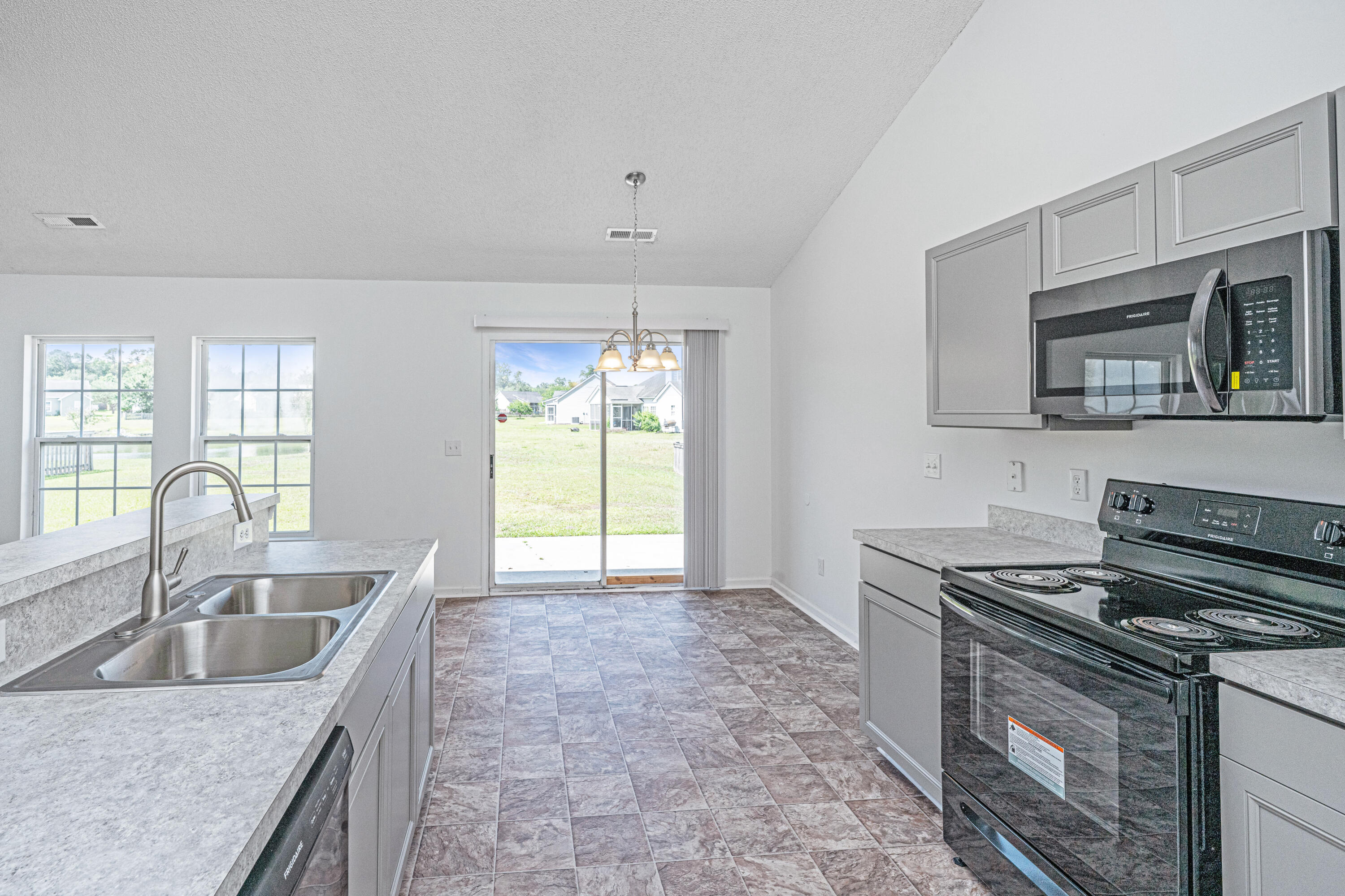 Vacant kitchen with gray cabinets, double-basin sink, electric range, and sliding door to the backyard.