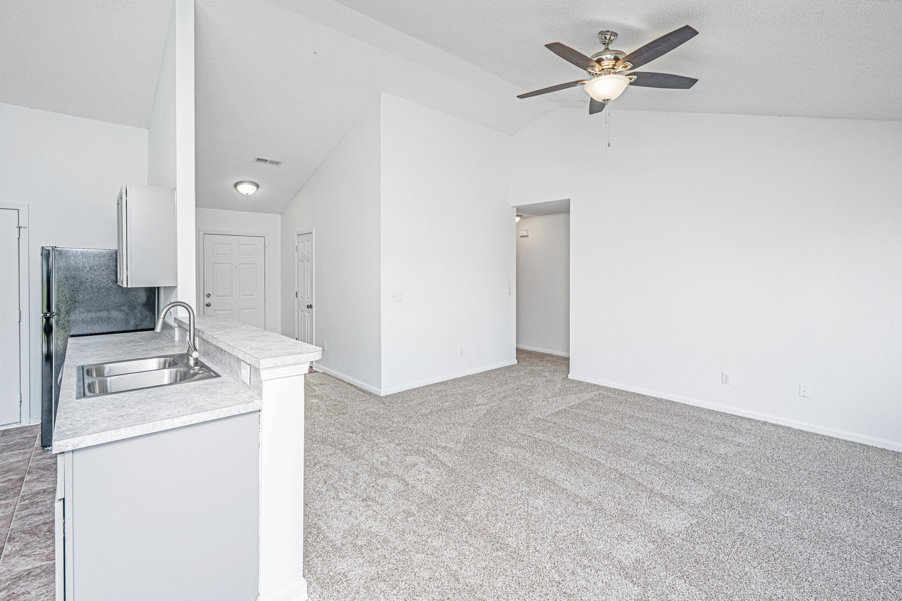 Open-plan kitchen and living area with a breakfast bar, carpet, and ceiling fan.