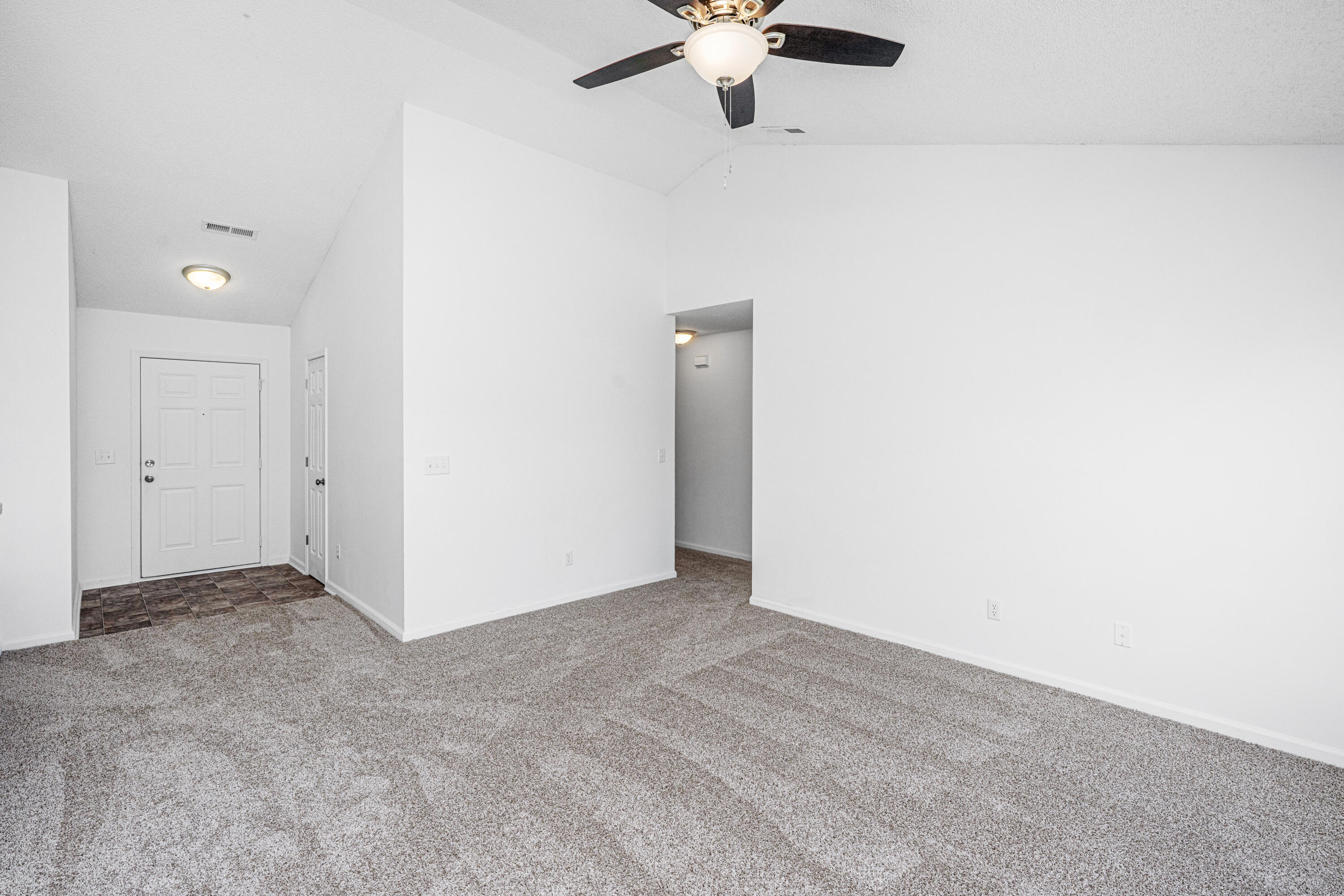 Empty living room with carpet, ceiling fan, and tiled entry by the front door.