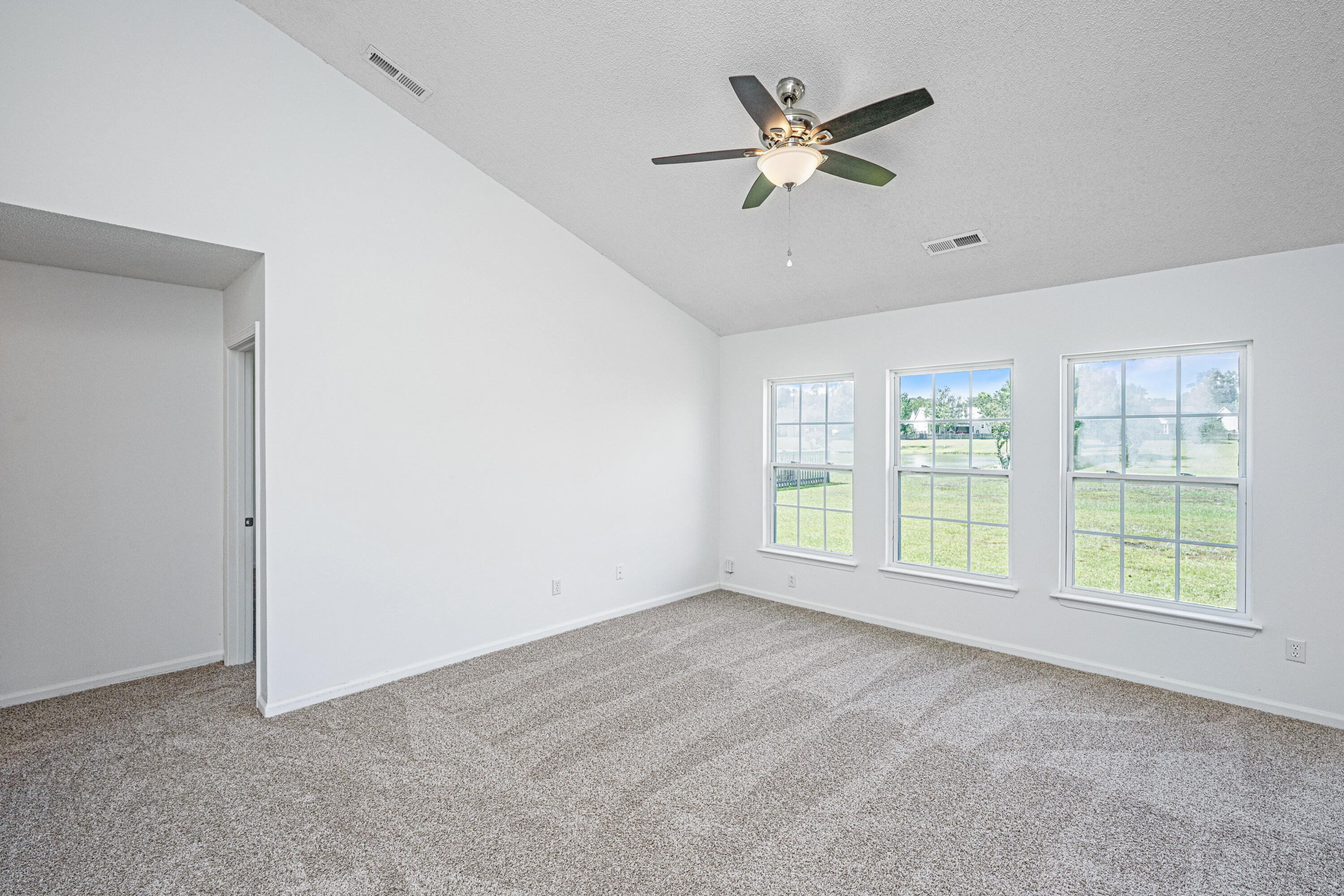 Vacant carpeted bedroom with three windows and a ceiling fan.