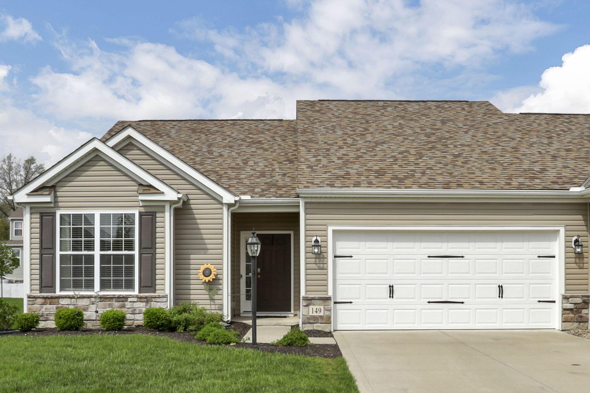 Beige single-story home with a white two-car garage, stone accents, and a green front lawn.