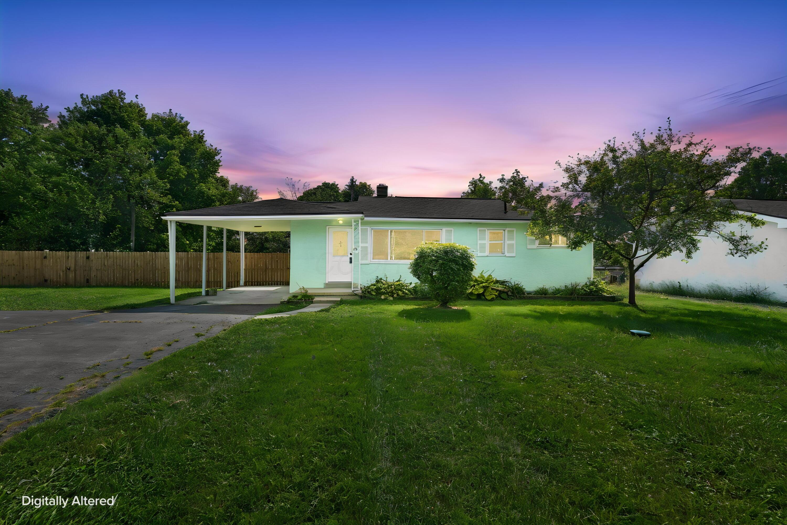 Mint-green single-story house with a covered carport and broad lawn at dusk.