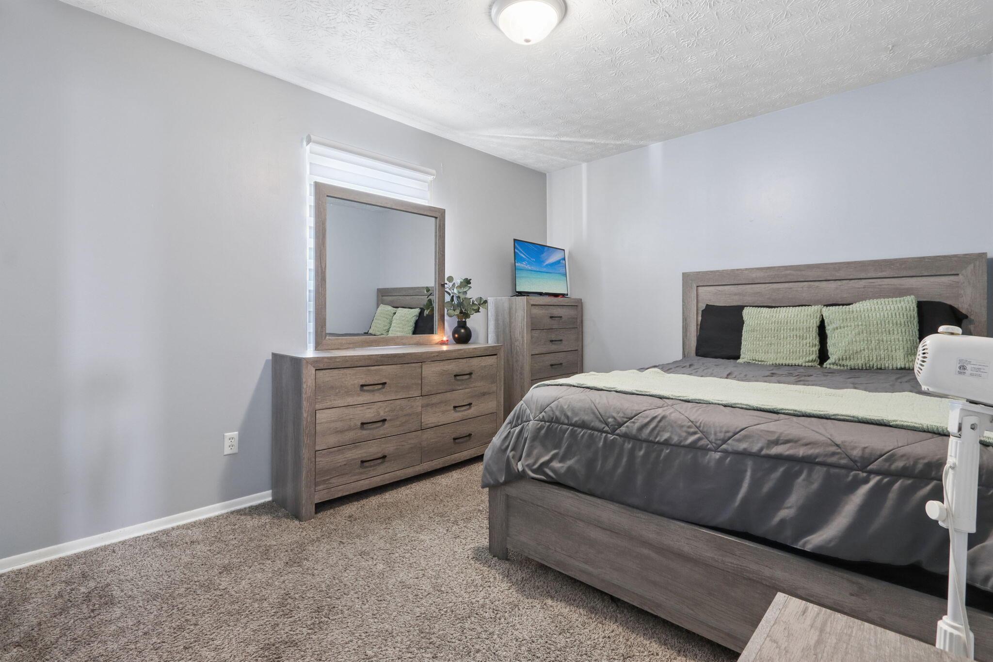 Bedroom with a gray bed, pale green pillows, and matching wooden dresser and mirror.