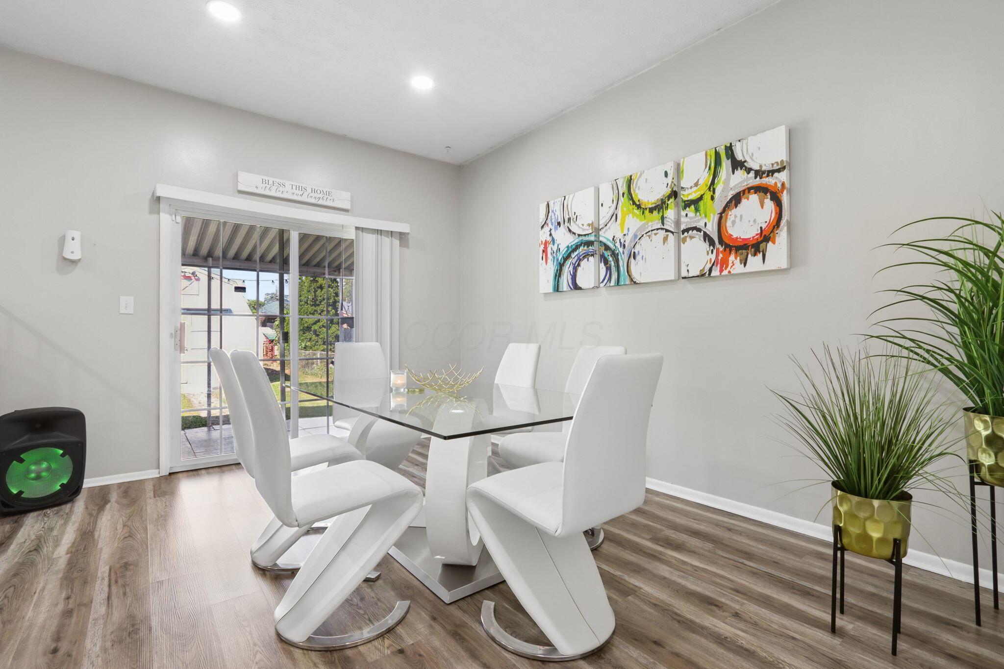 Dining room with a glass-top table, white chairs, colorful abstract art, and sliding glass doors.