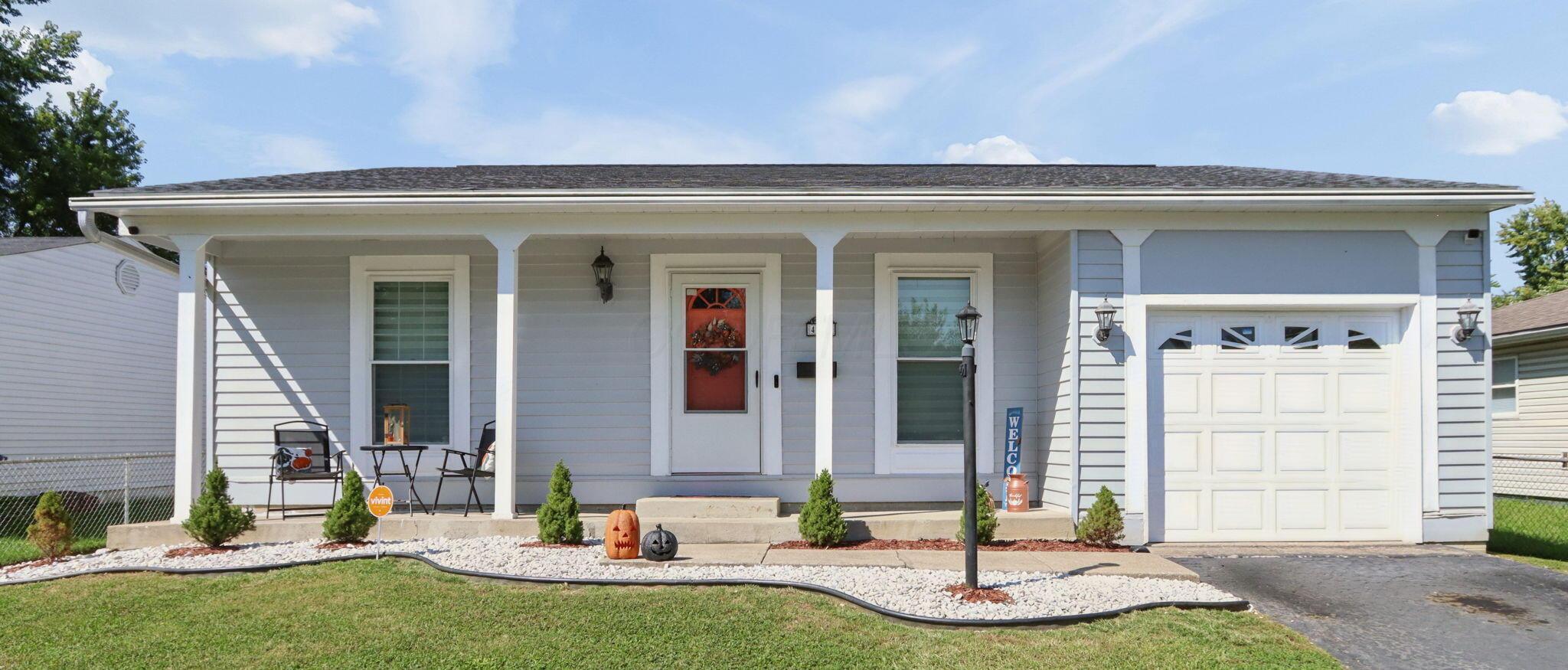 Gray ranch home with a covered porch, white garage, and Halloween pumpkins by the front walk.