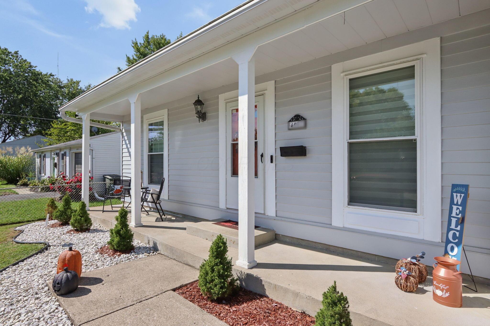 Light gray house with a covered front porch, white columns, and seasonal decorations by the entry.