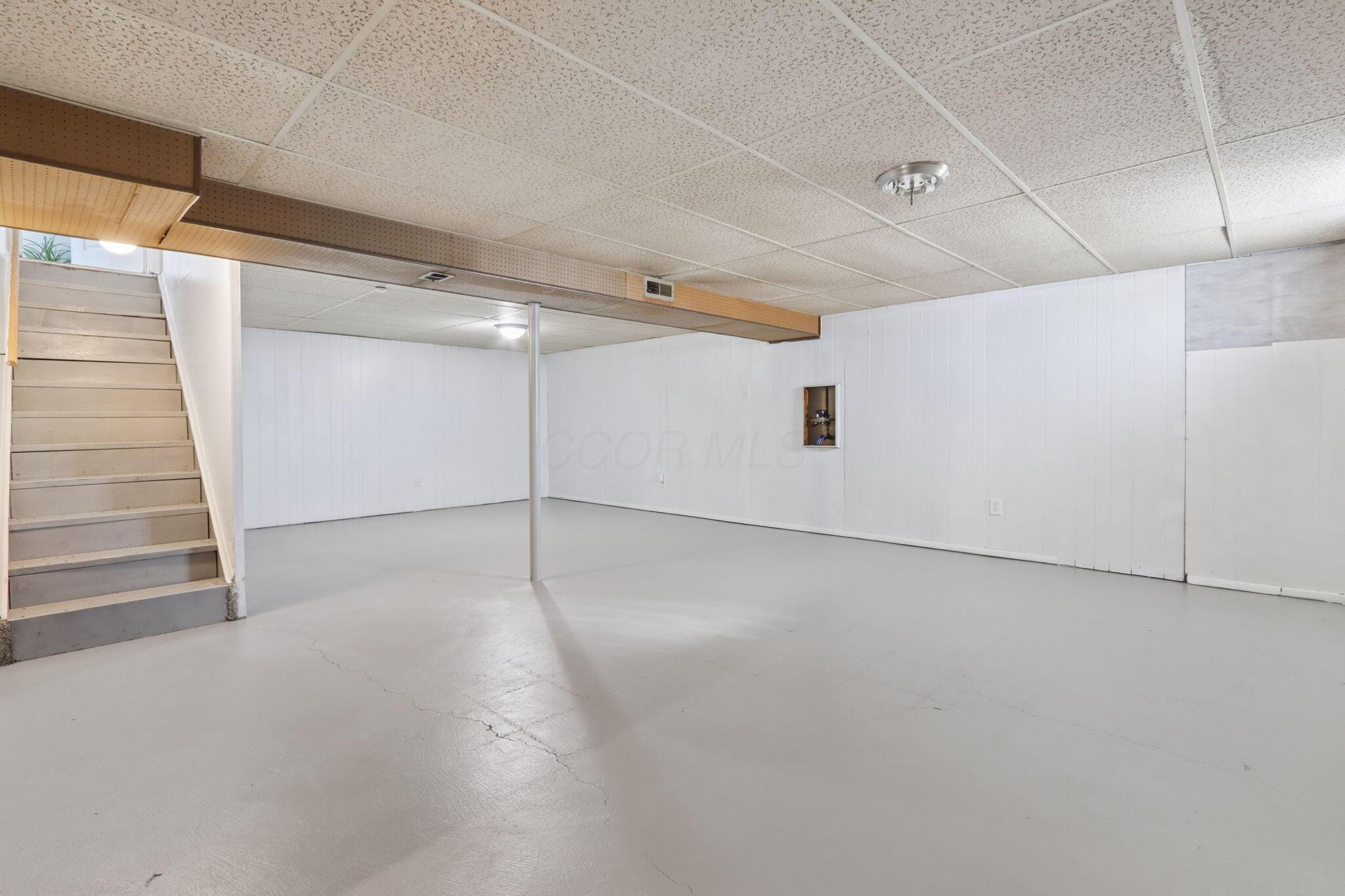 Empty basement with a concrete floor, white paneled walls, and stairs along one side.