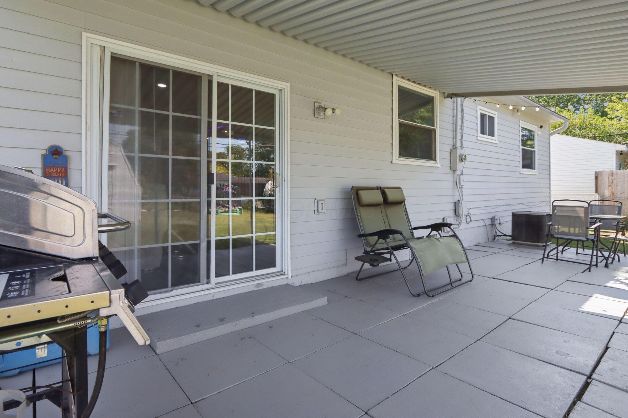 Covered patio with paver flooring, reclining chairs, a dining set, and a grill beside a sliding glass door.