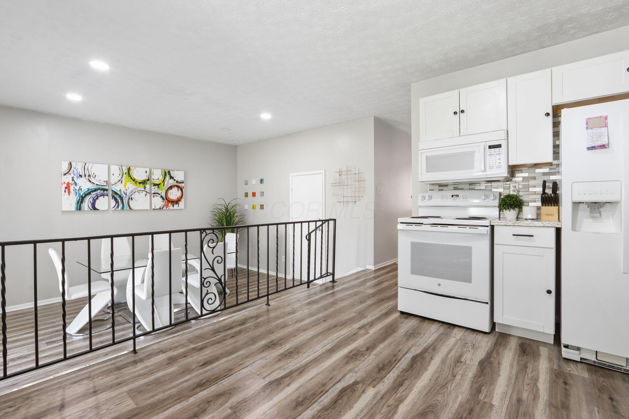 Kitchen and dining area with white appliances, a dining set, and a black metal railing.