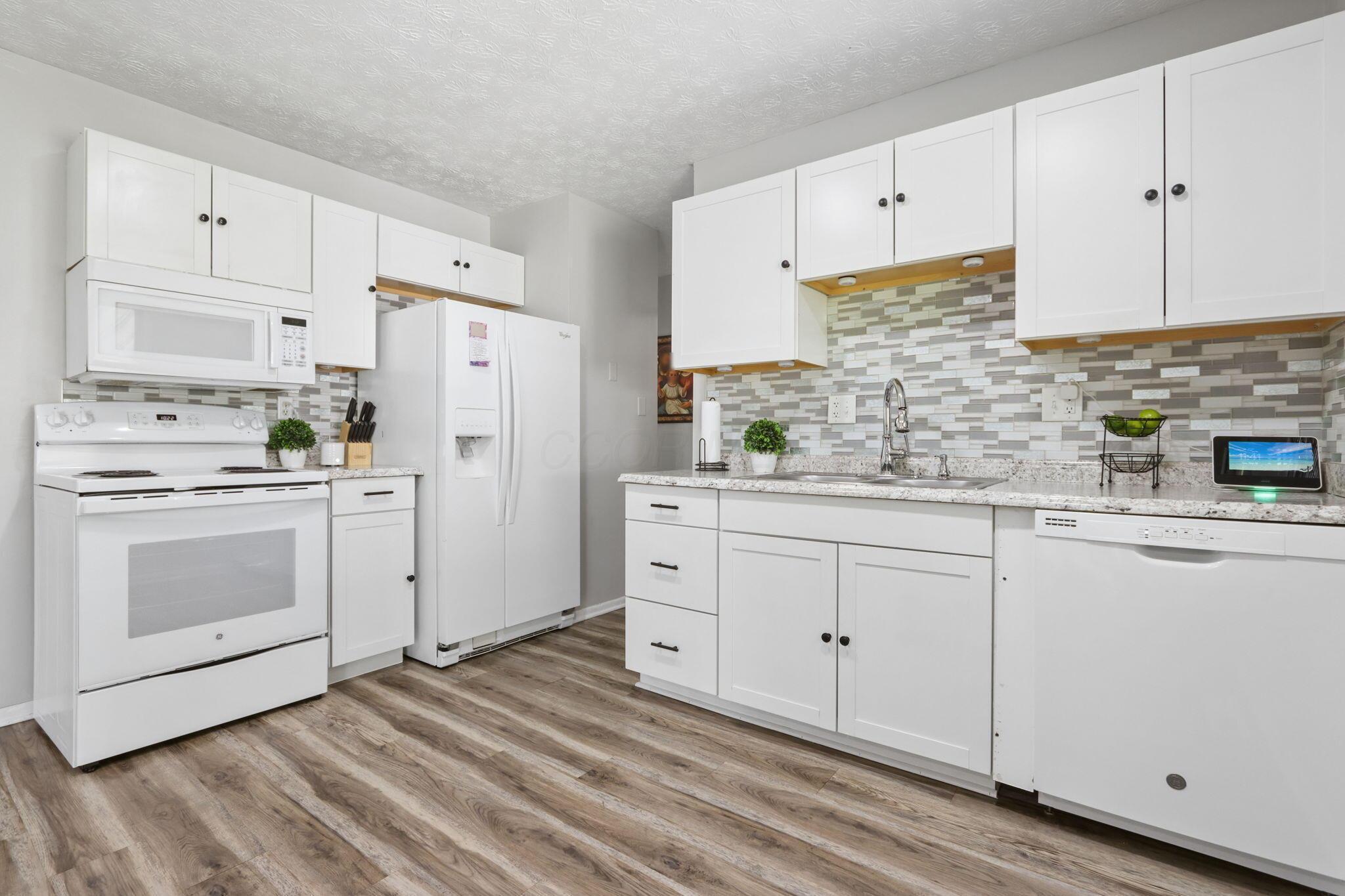 Bright kitchen with white cabinets, a mosaic tile backsplash, and wood-look floors.