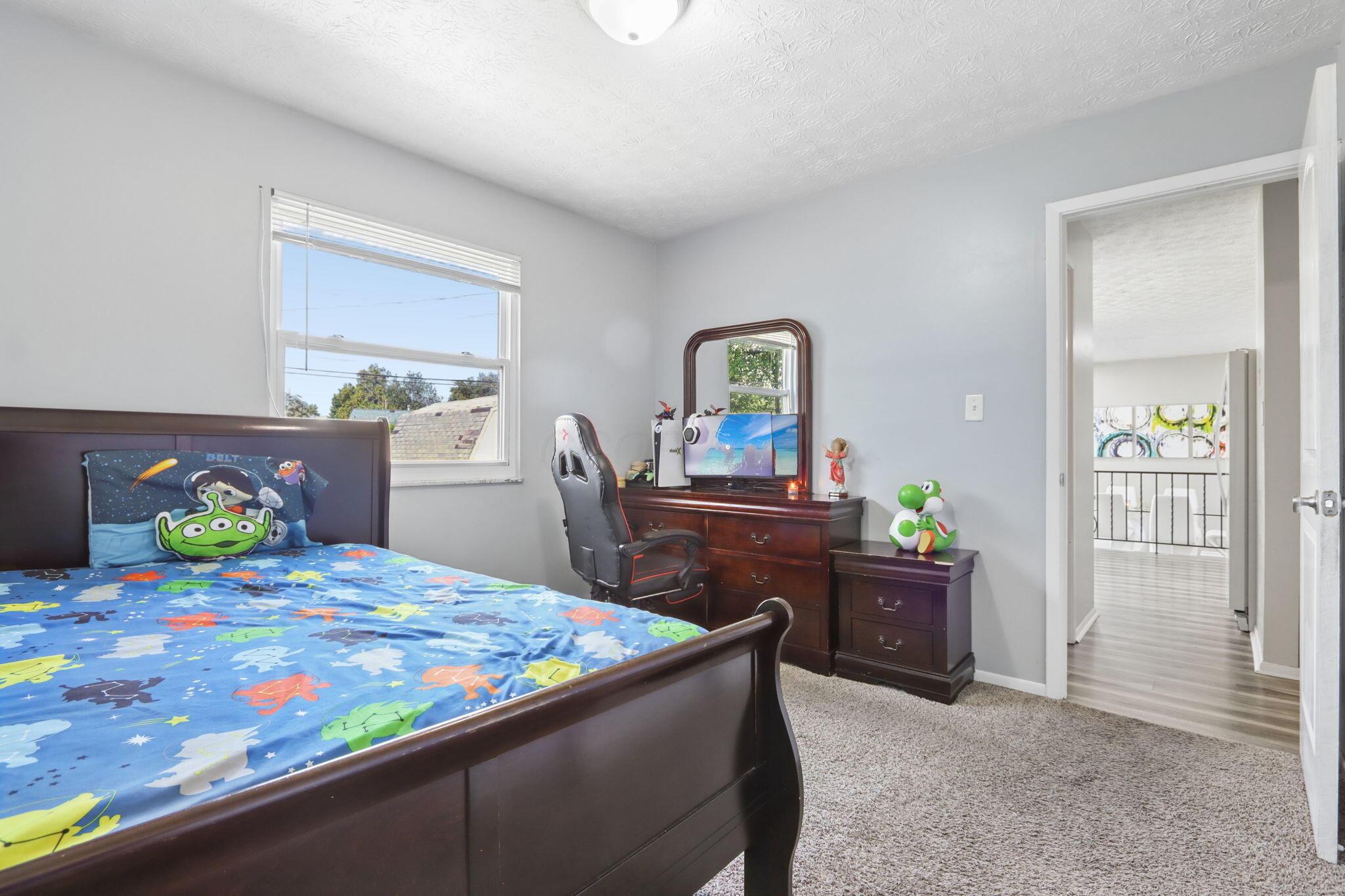 Bedroom with blue character-print bedding, dark wood furniture, and a desk with a gaming chair.