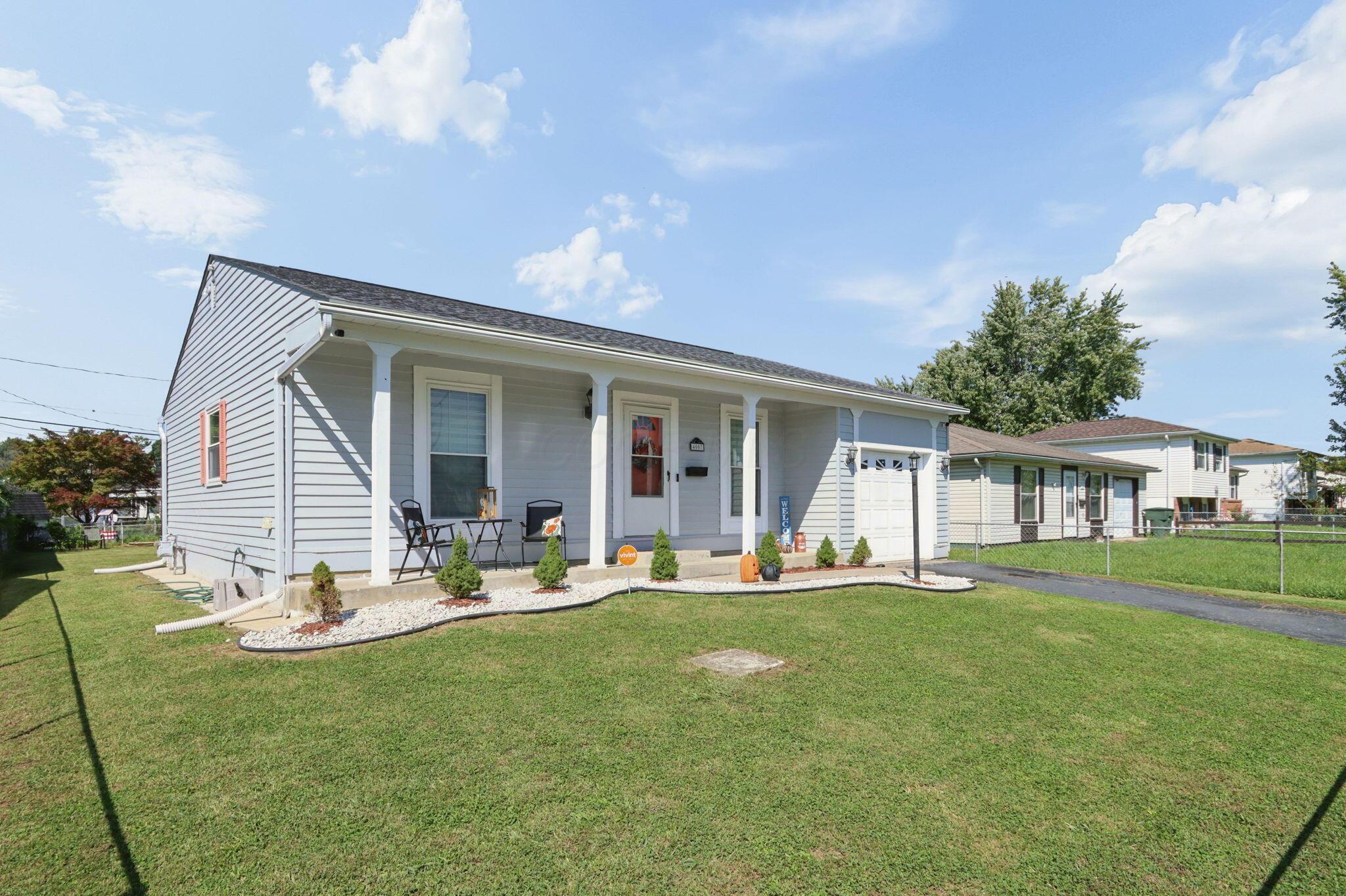 Gray single-story house with a covered porch, attached garage, and landscaped front lawn.