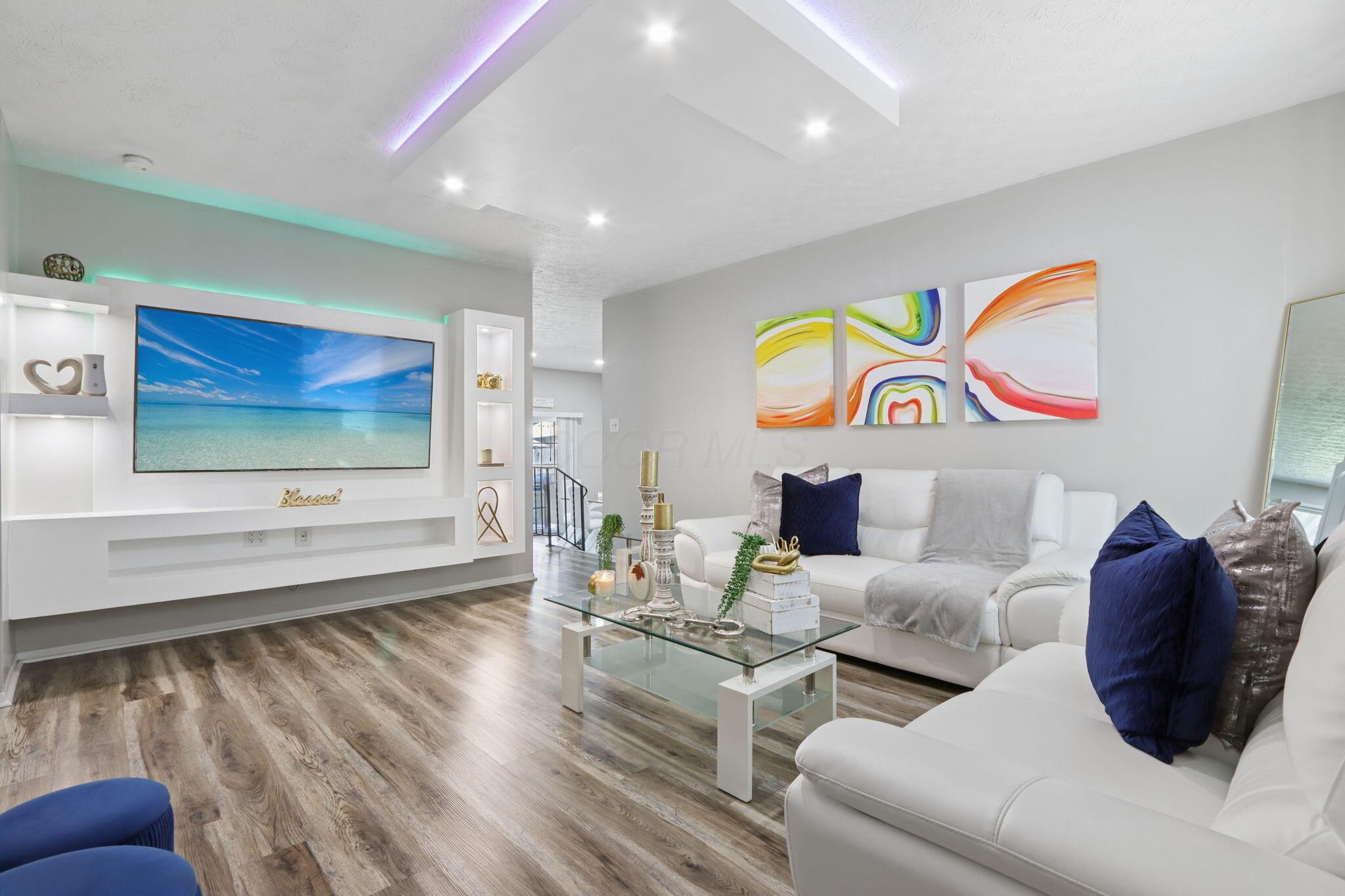 Living room with white sectional sofas, navy cushions, and a built-in TV wall with accent lighting.