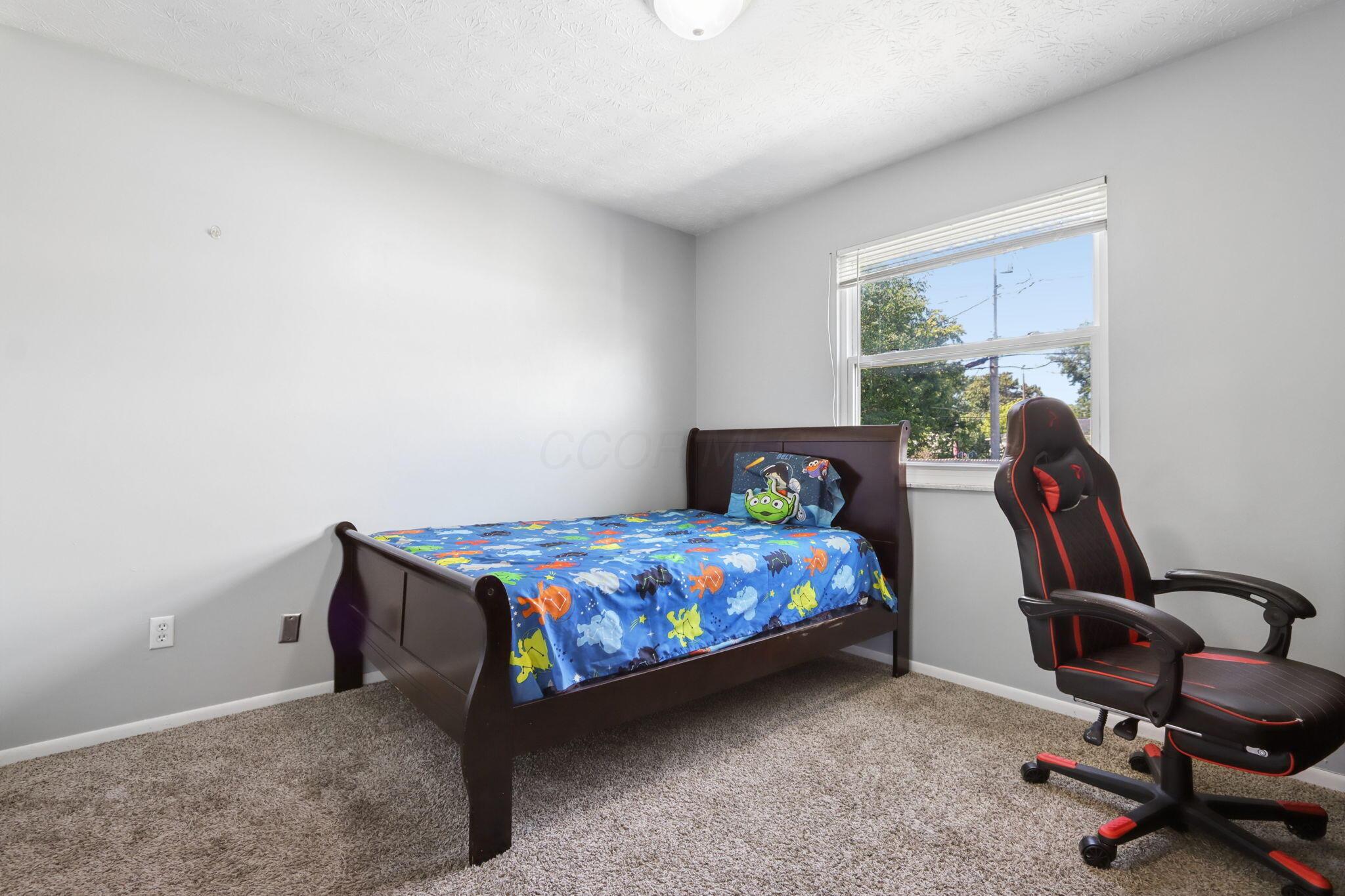 Bedroom with a dark wood twin bed, blue fish-patterned bedding, and a black-and-red gaming chair.