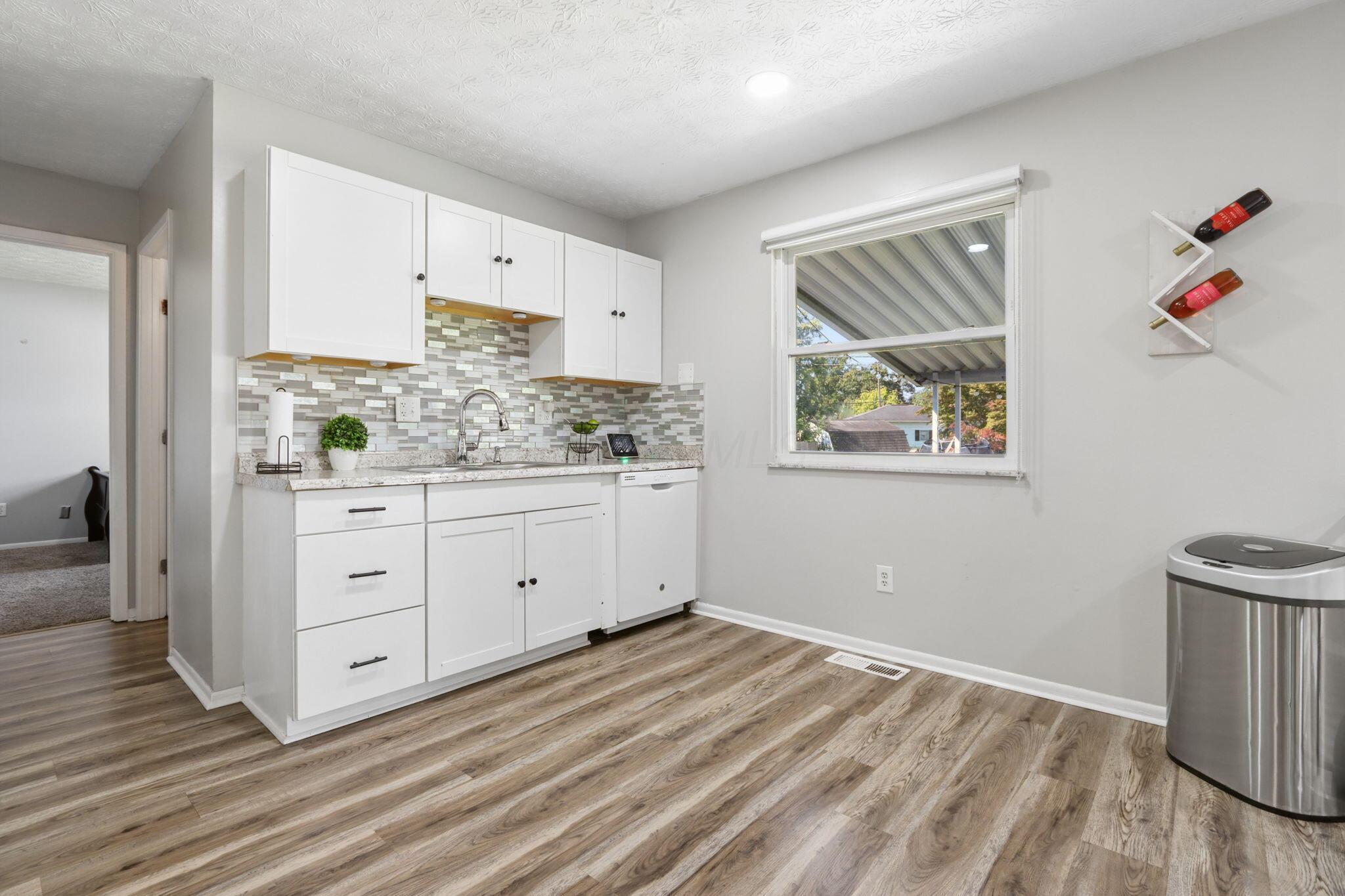Kitchen with white cabinets, patterned tile backsplash, and a window overlooking the yard.